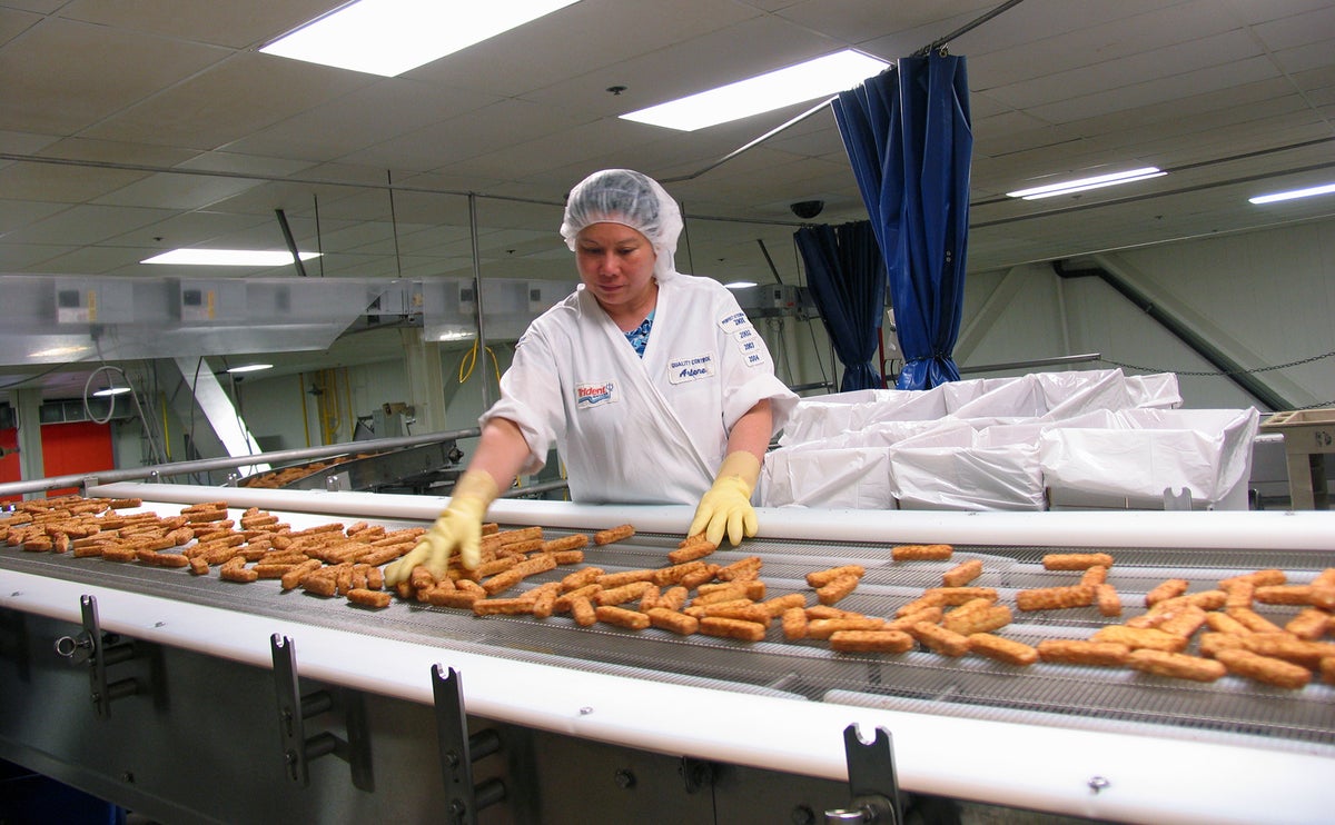 A Trident Seafoods employee shorts freshly made Ultimate Fish Sticks on a conveyer belt at its Anacortes location