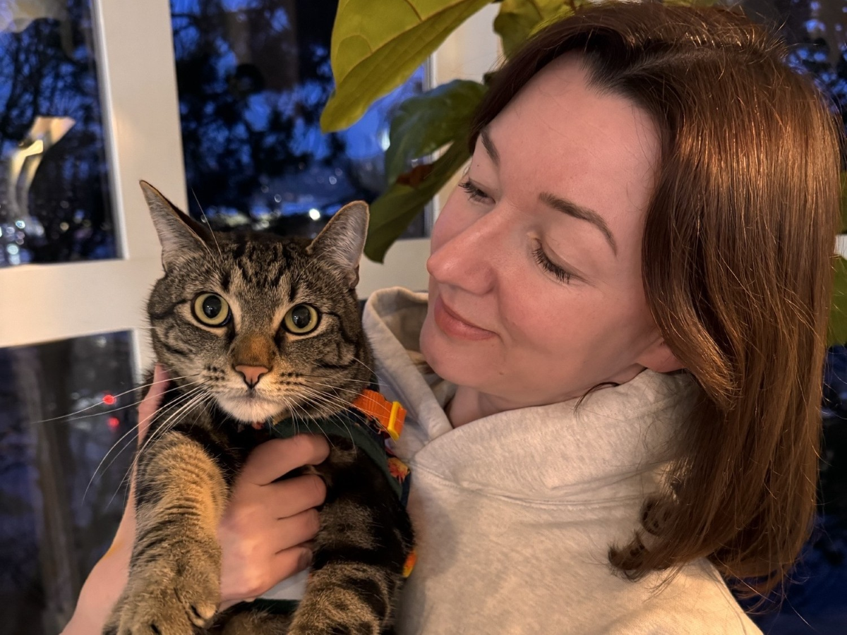 Olga hugging her cat Orion, looking at it with a smile. 