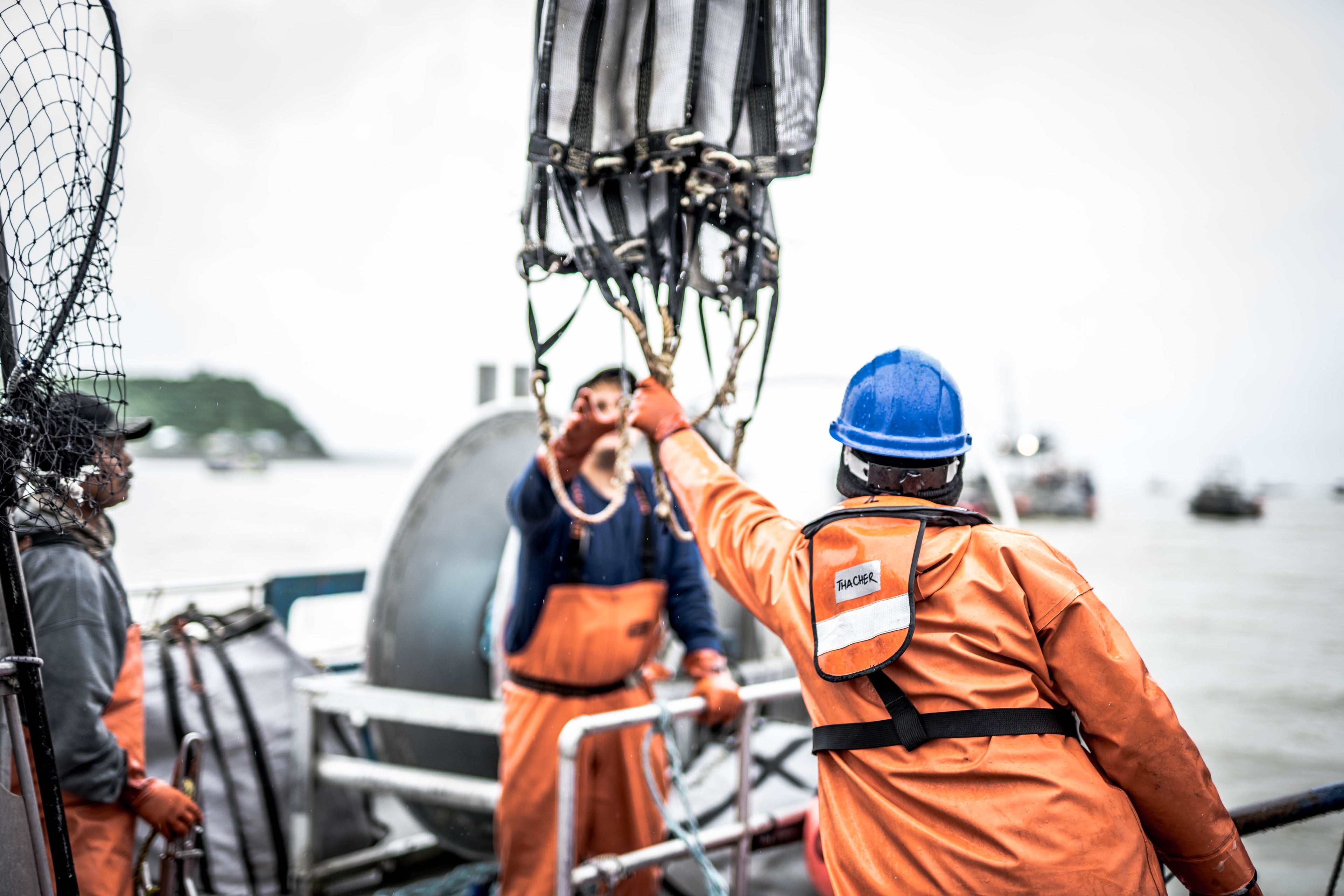 Two people helping each other pass some rigging across