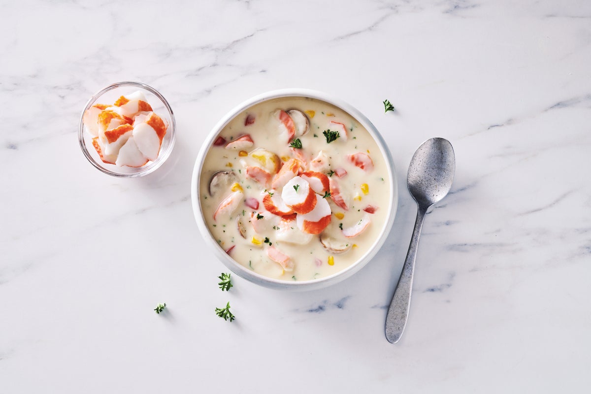 Surimi seafood chowder in a bowl with a spoon on the side on a marble table