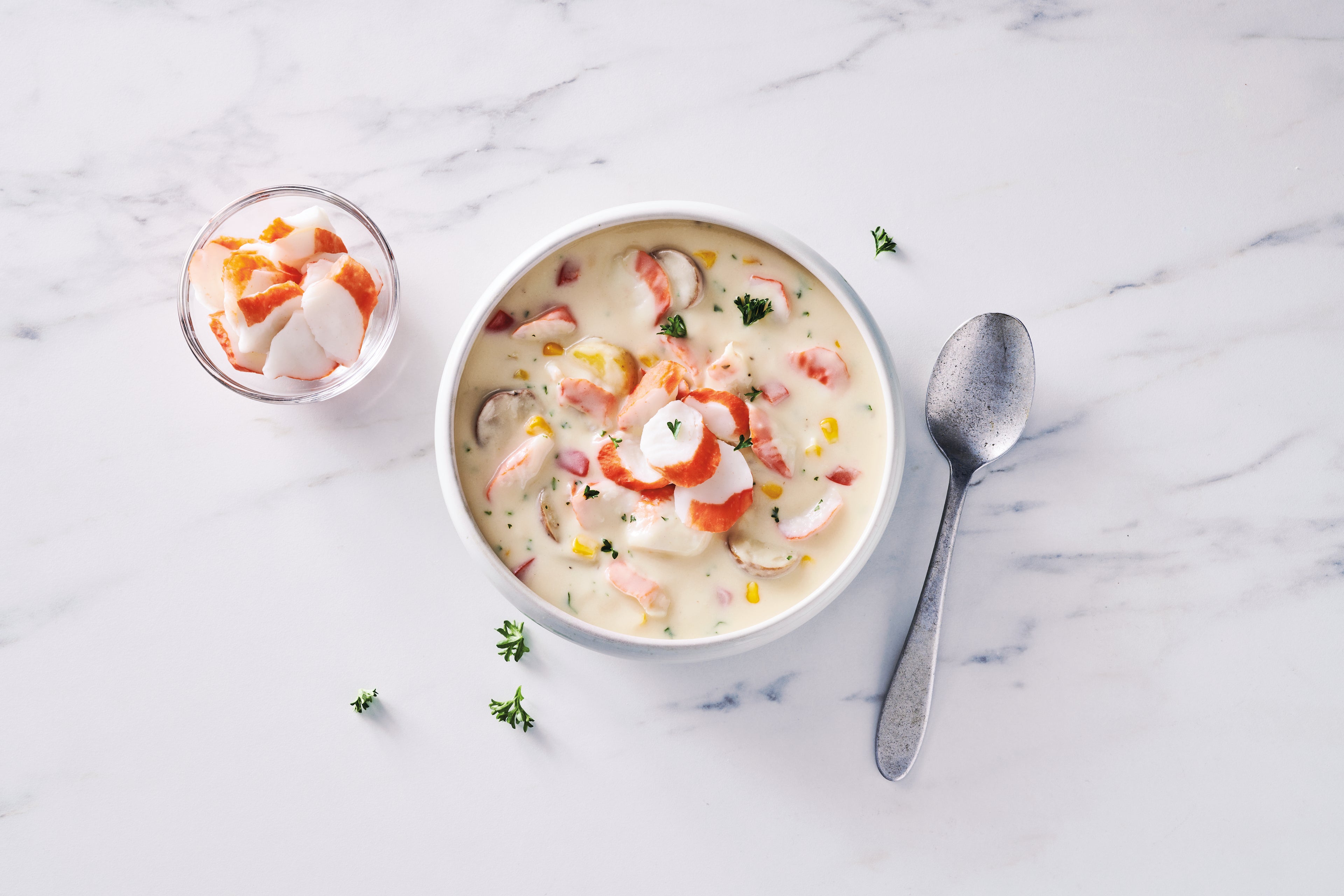 Surimi seafood chowder in a bowl with a spoon on the side on a marble table