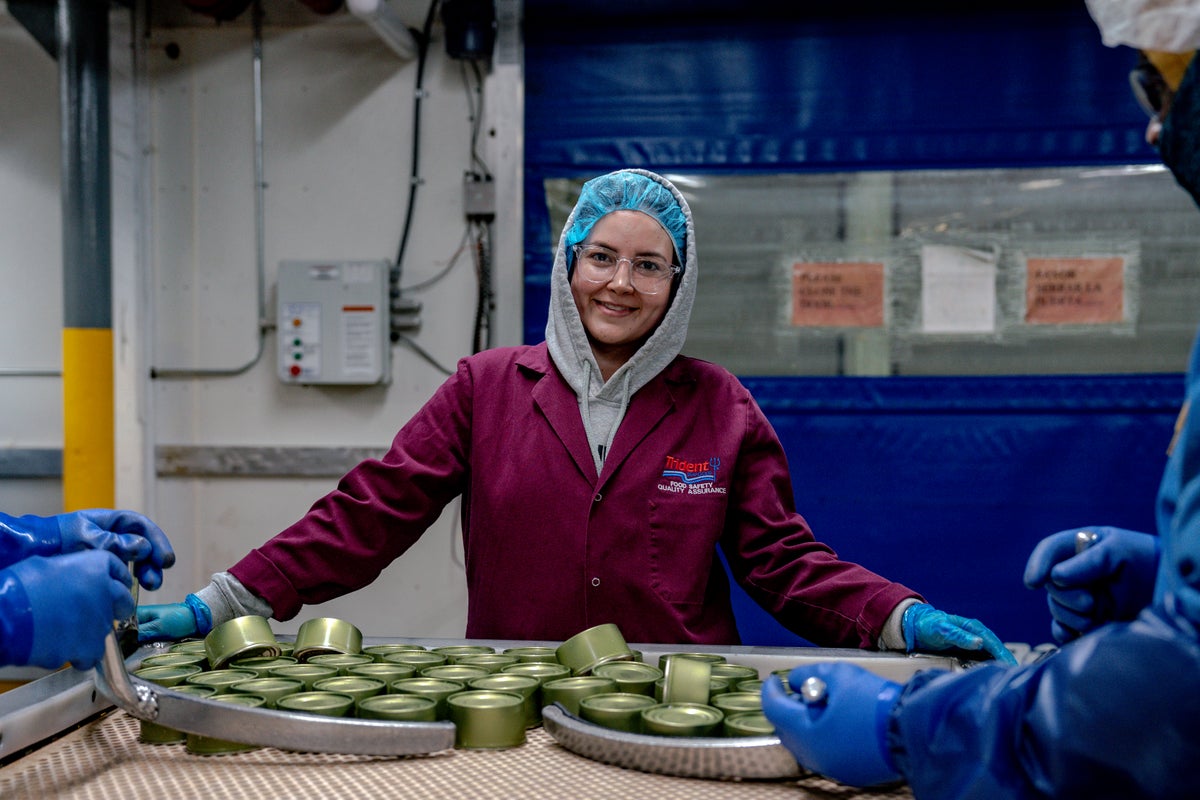 Woman working in salmon canning plant, smiling. 
