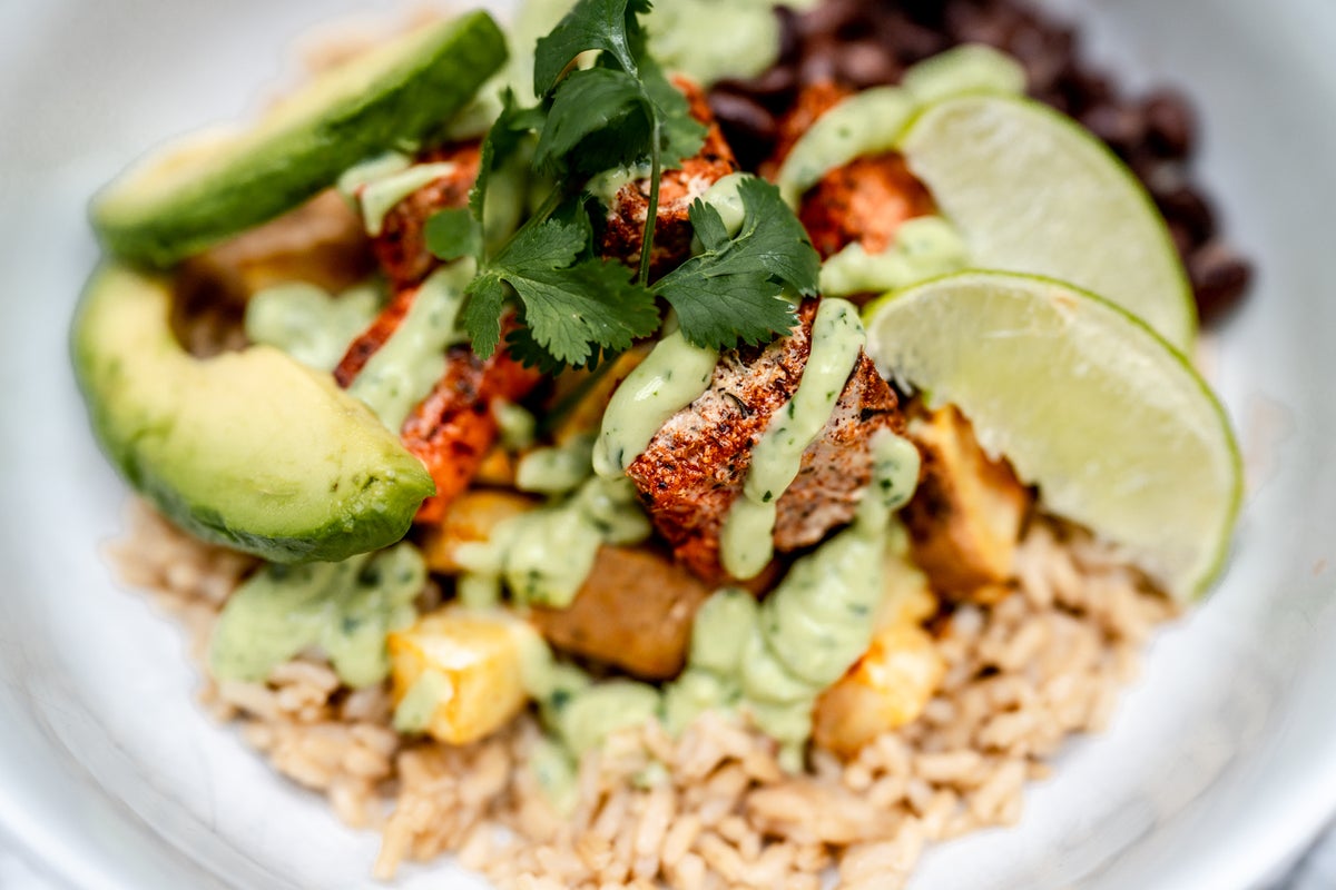 Wild Alaska salmon sits on top of a bed of rice, drizzled in an avocado sauce and served with sweet potatoes. 