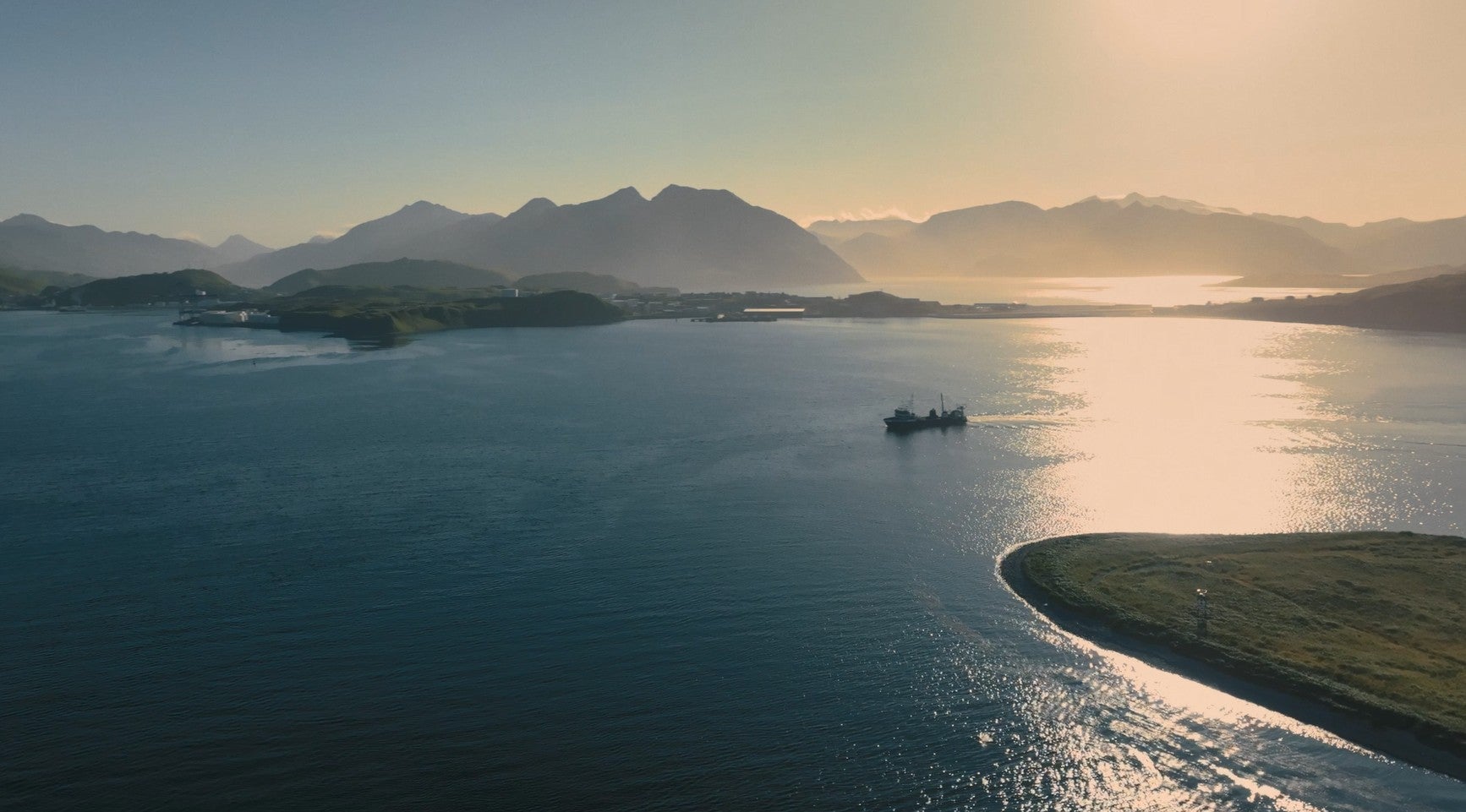 A commercial fishing vessel navigating open coastal waters at golden hour in Alaska. 