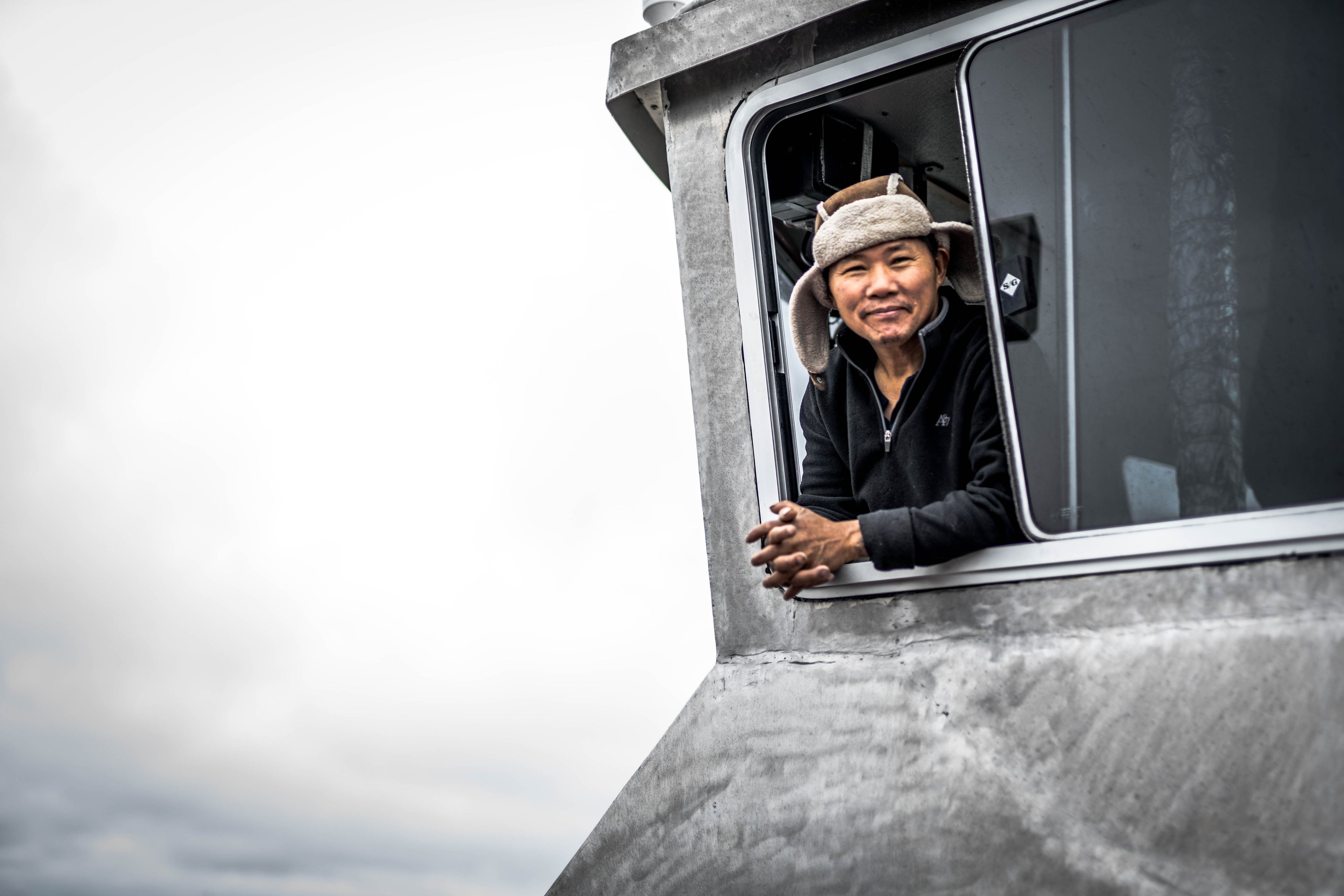 Man standing in wheelhouse of boat with head out the window