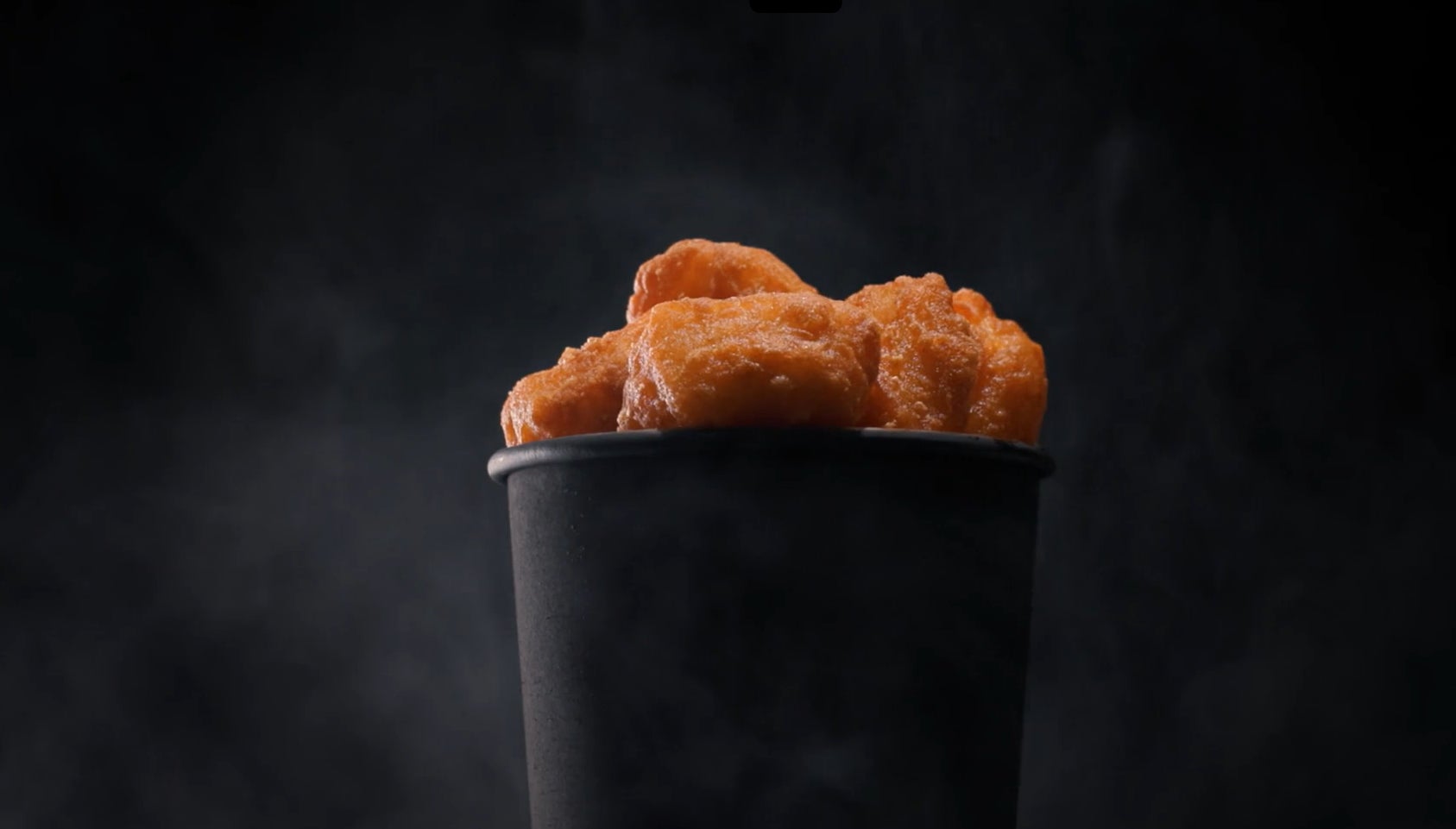 Crispy sauceable wild Alaska pollock nuggets in a black bucket against a black backdrop. 
