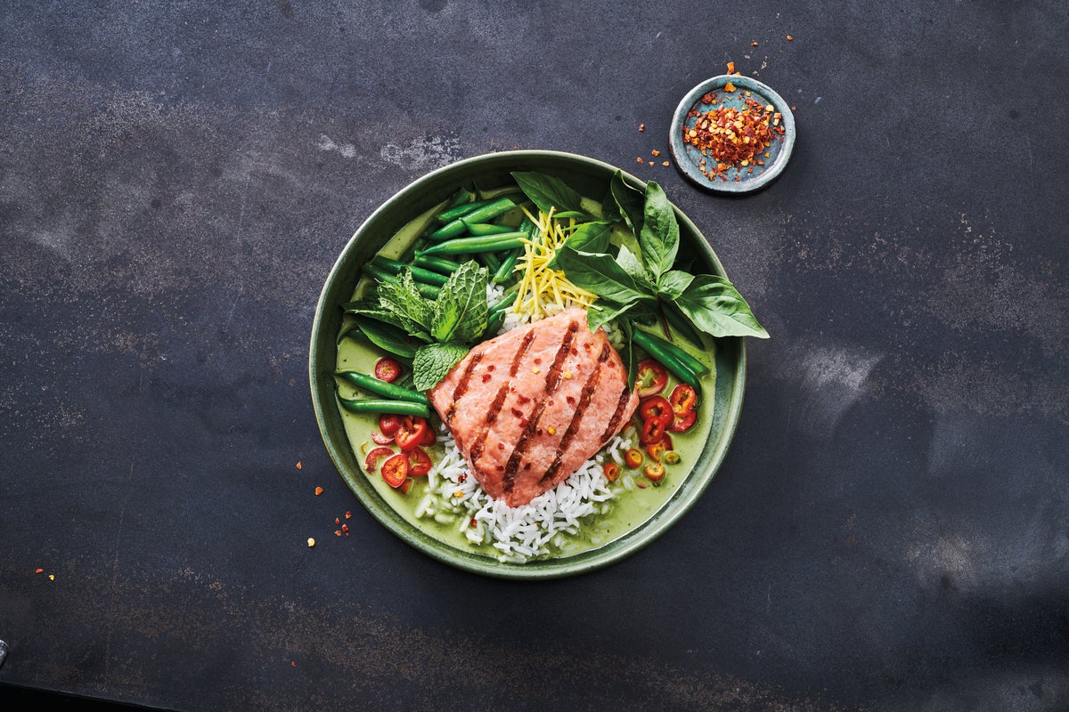 Redi Grilled Salmon fillet on a bed of rice, accompanied with various other vegetable and garnishes including sliced small red peppers. 