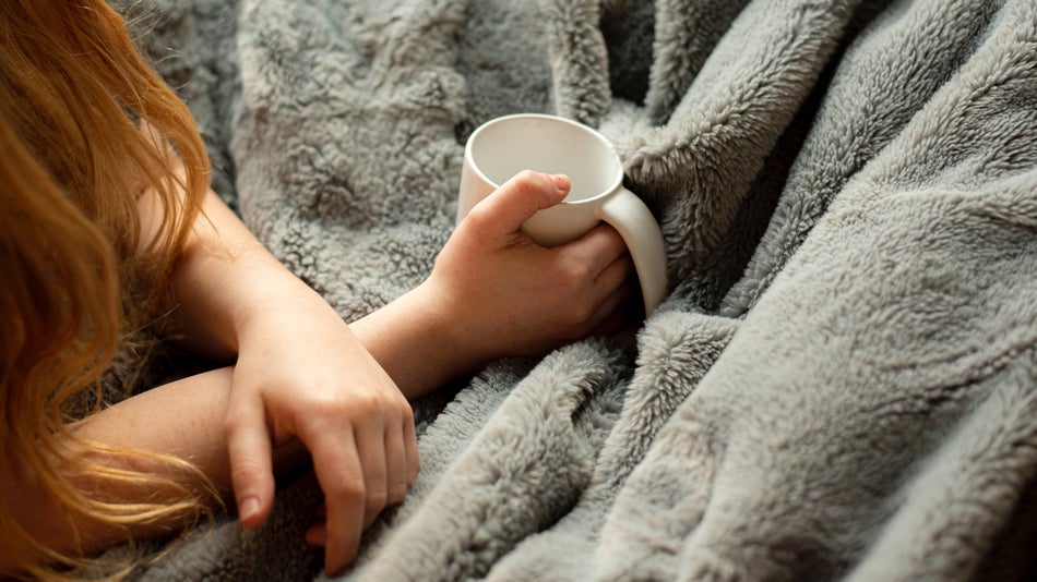 Woman having a beverage under a cozy throw blanket
