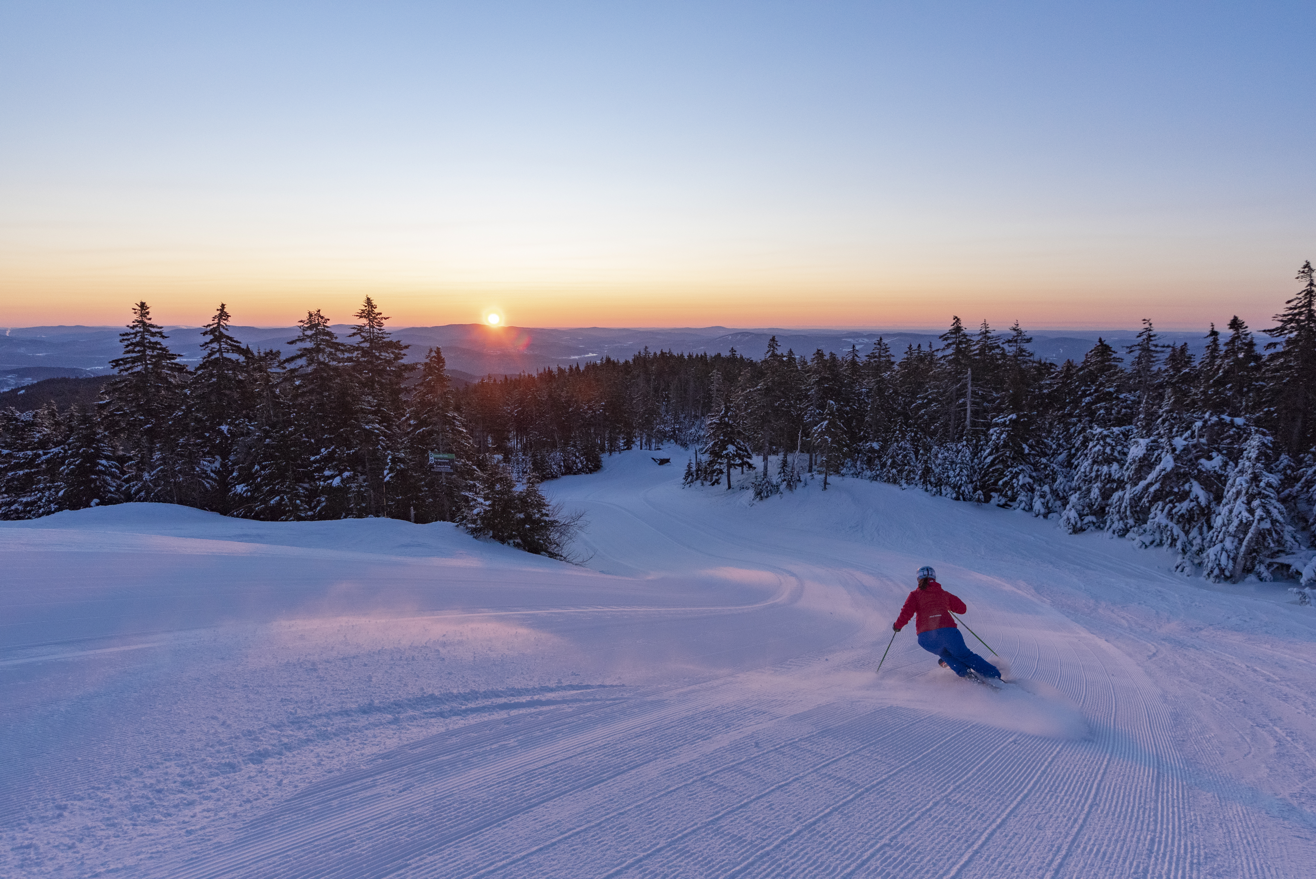 Skiing down groomed run as sun comes up over the mountains