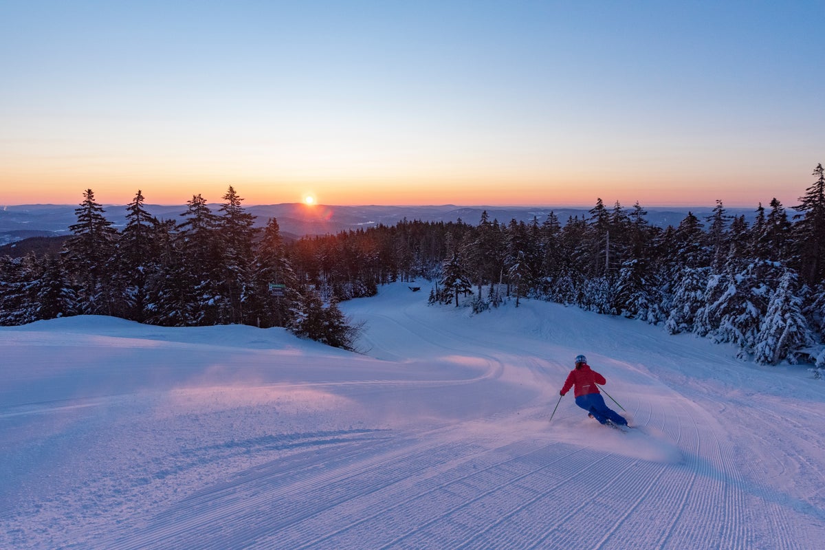 Skiing down groomed run as sun comes up over the mountains