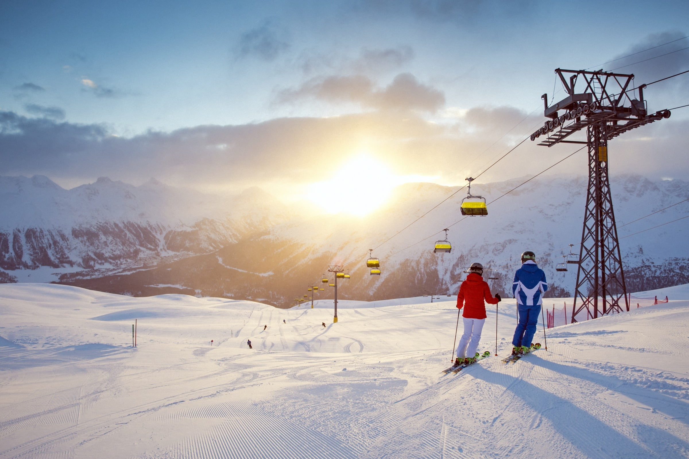 Two people taking a break on ski slopes in St. Moritz while sun sets over mountains