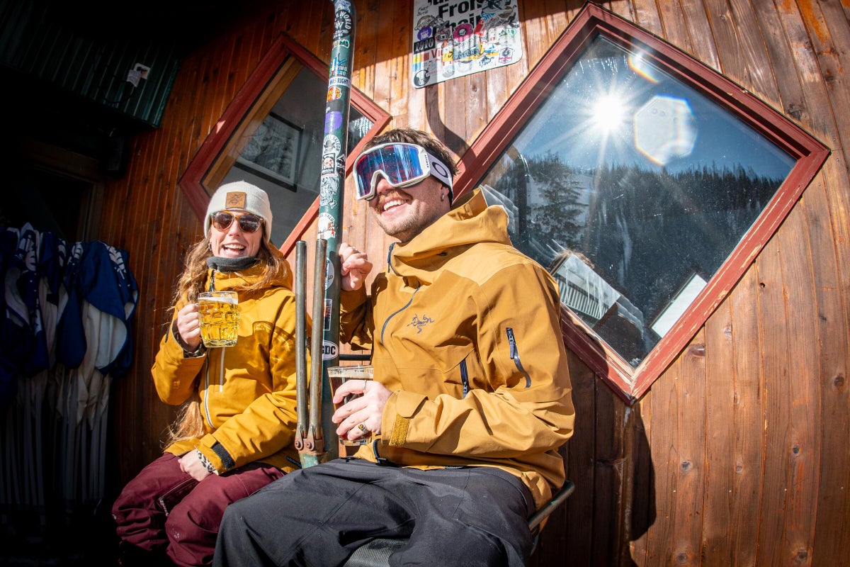 Couple sitting next to one another on bench outside of bar having a beer