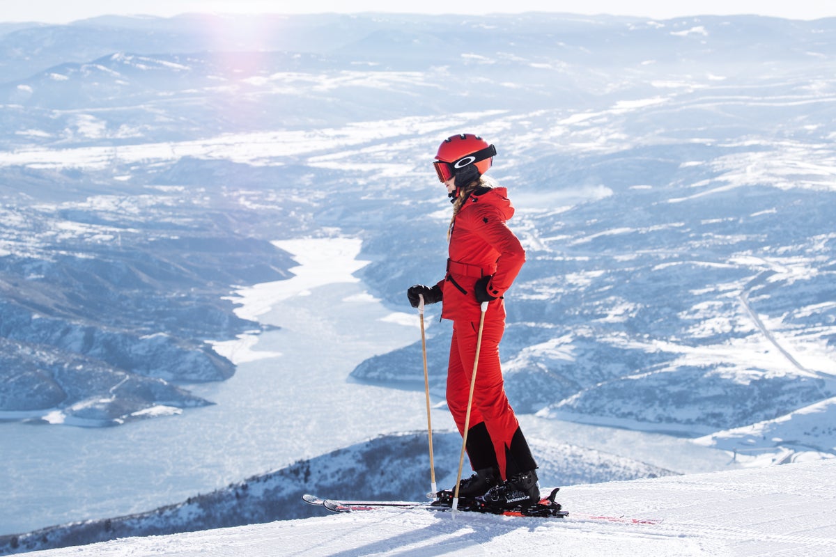 Deer Valley Resort skier standing by lake in red ski outfit.