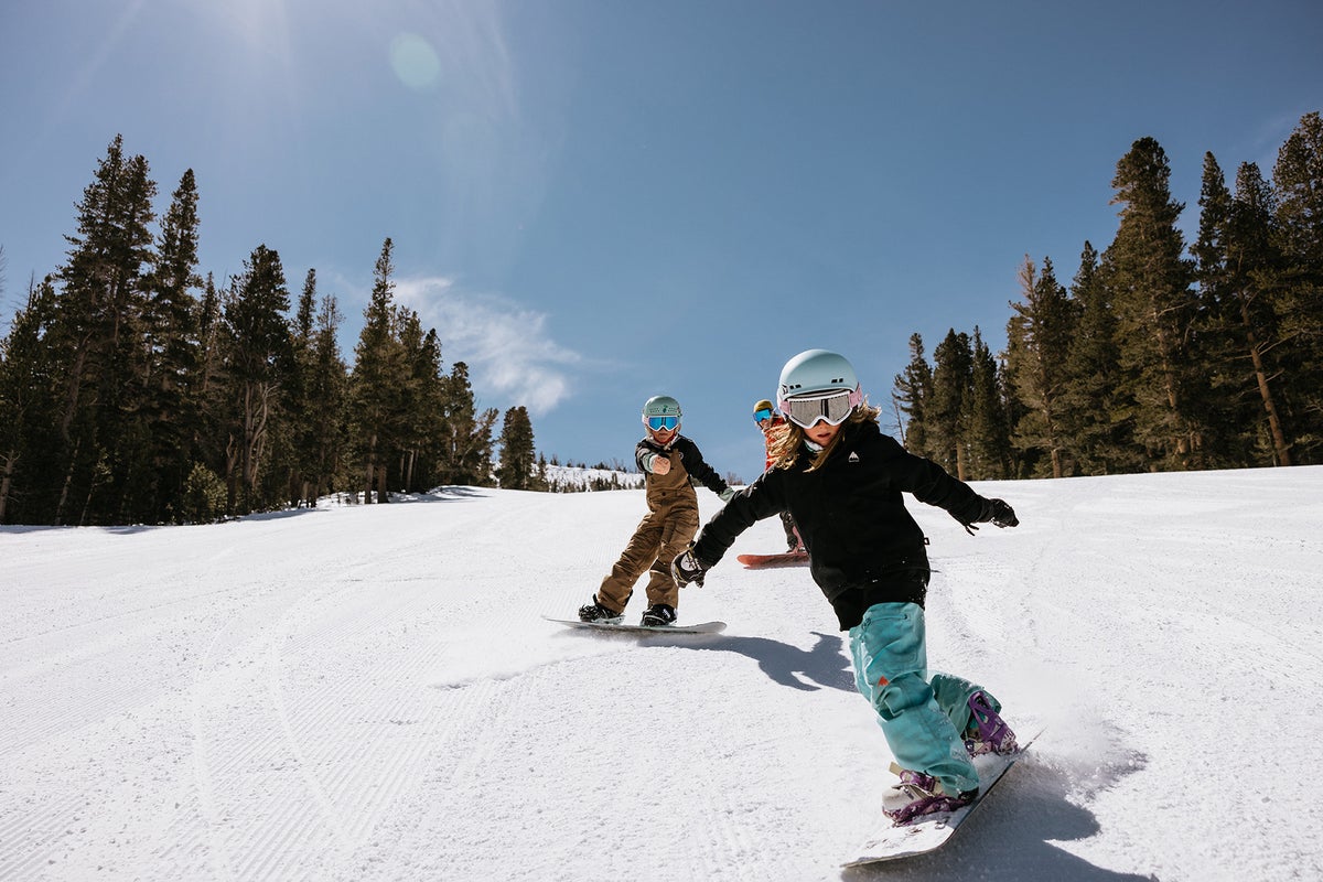 Kids snowboarding down groomed run on a sunny day at Mammoth Mountain