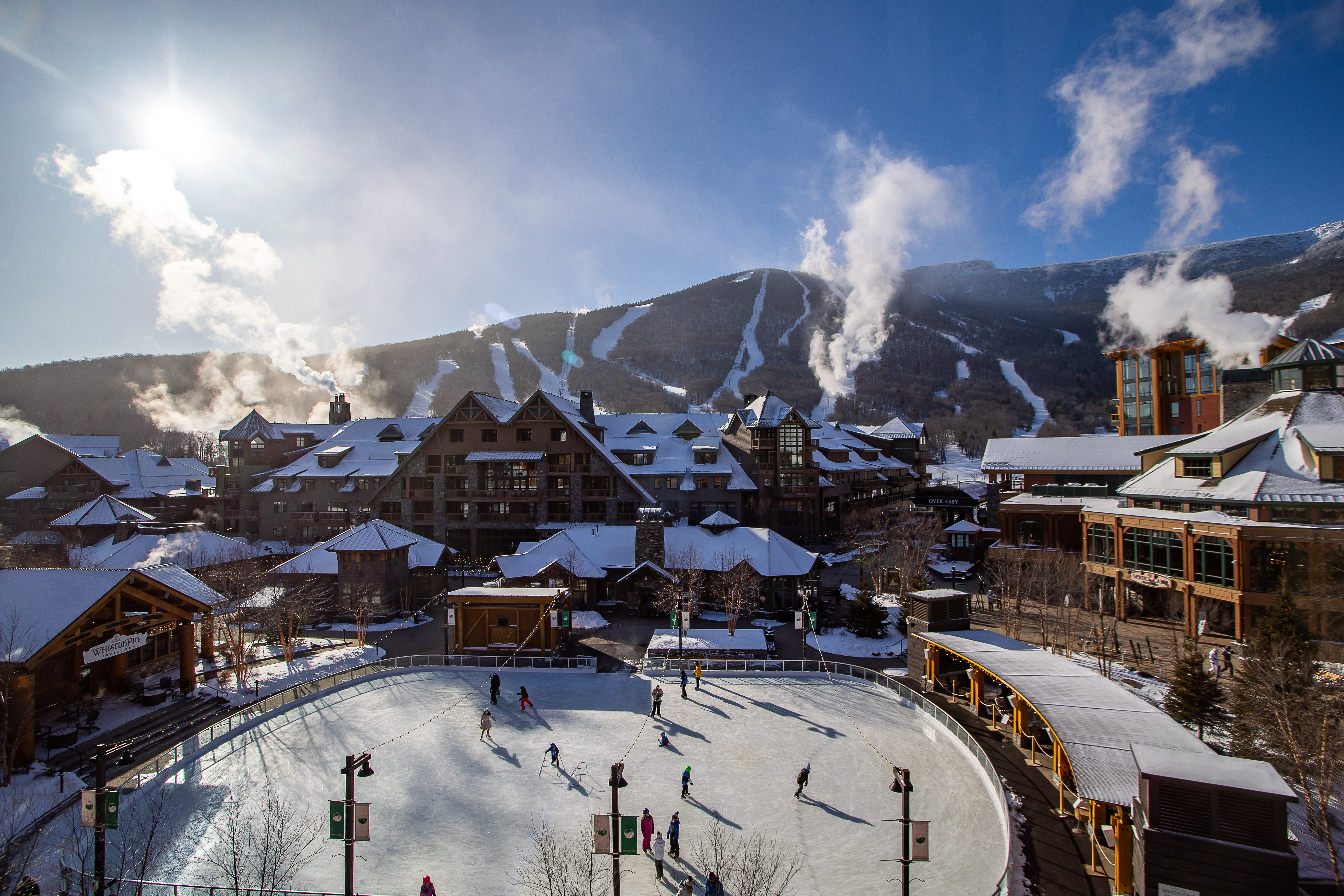 Sunny day at Stowe Mountain Resort where people are skating on ice rink