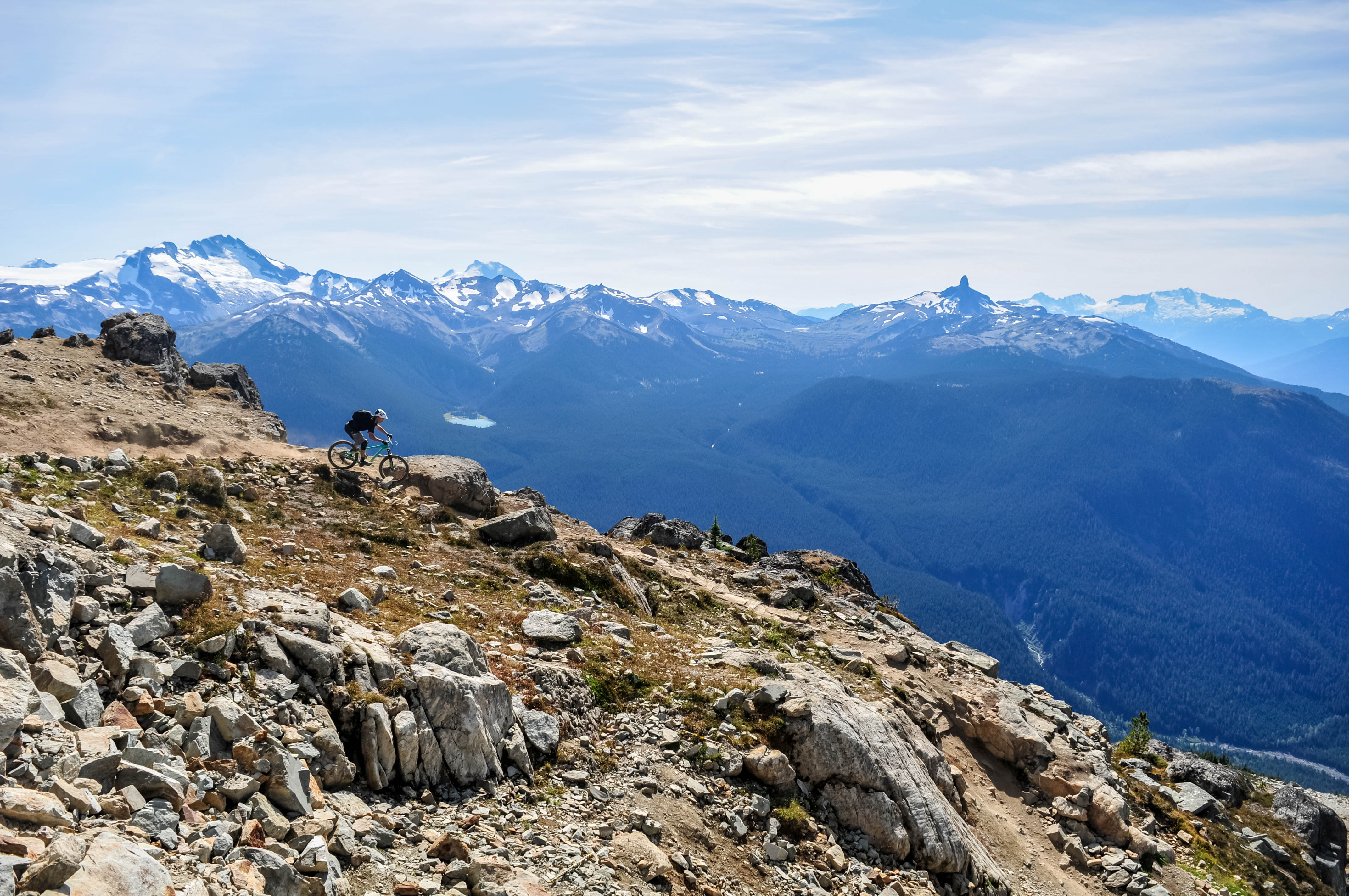 Person biking down rocky trail with mountains behind them.