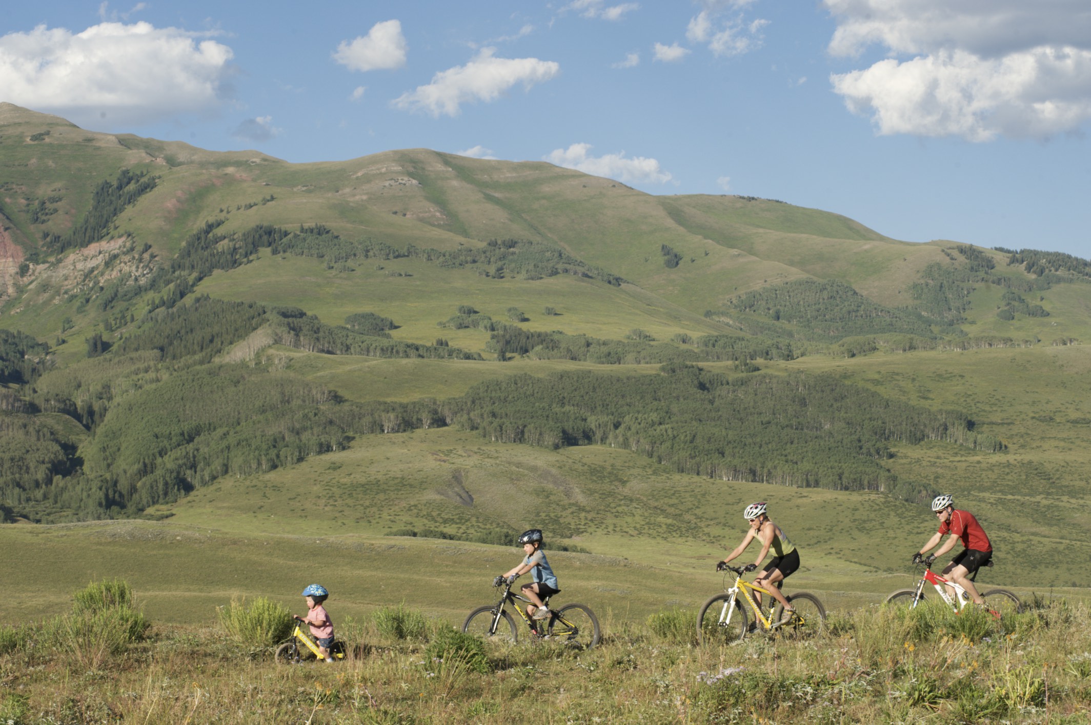Family riding down trail with green mountains behind them.