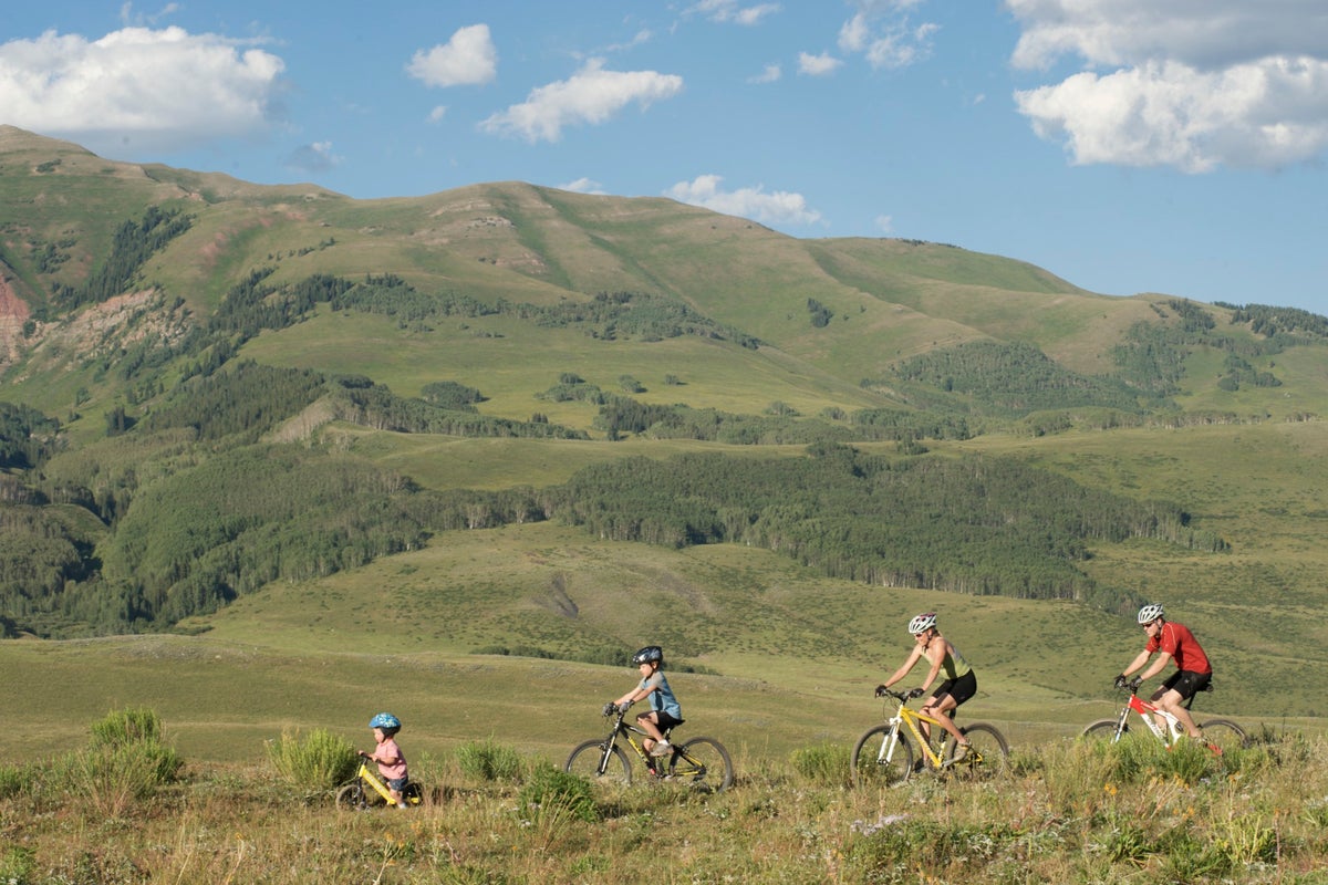 Family riding down trail with green mountains behind them.