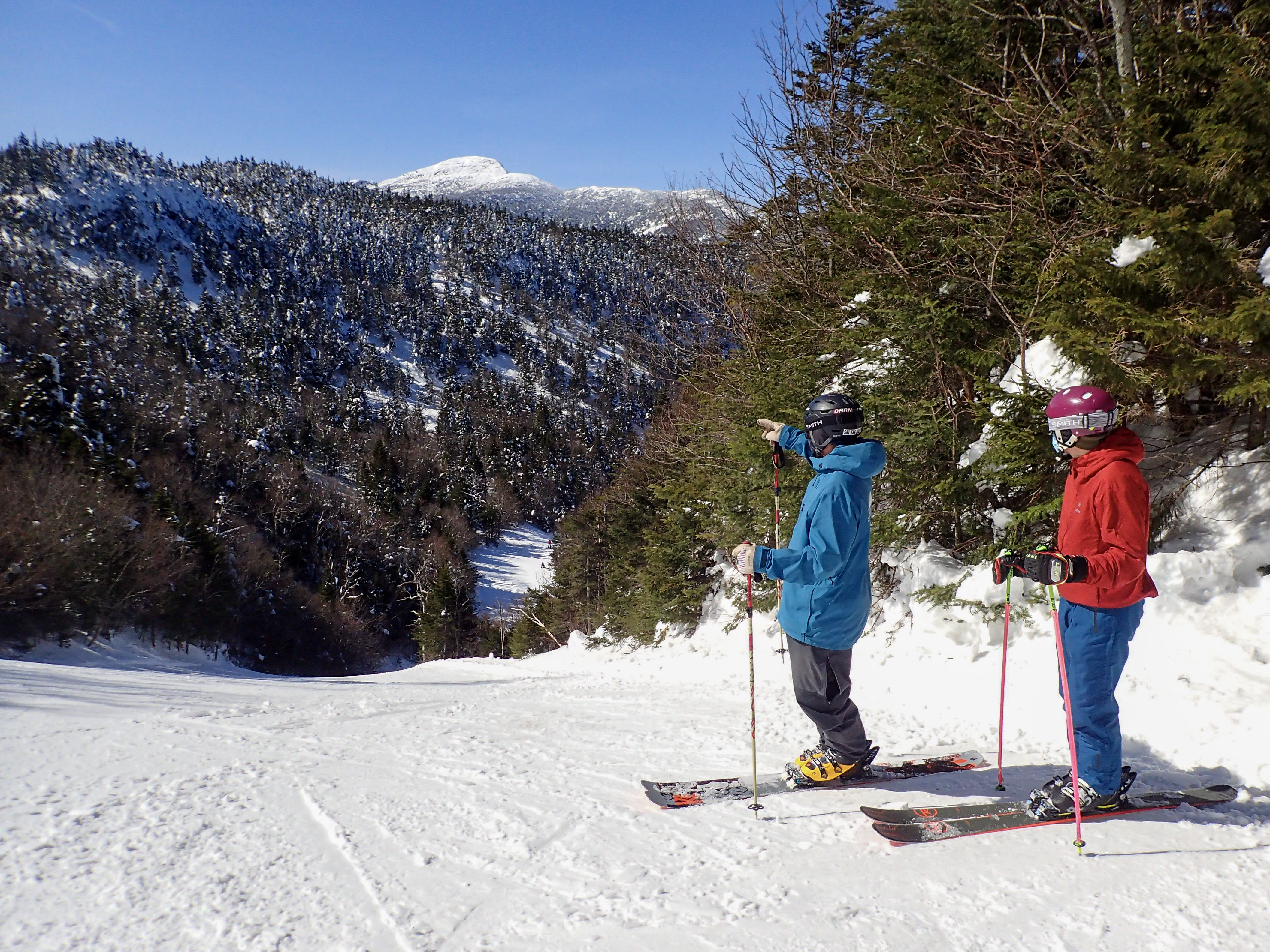 Two people at top of groomed slope at ski resort taking a break