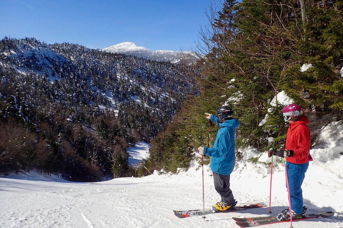 Two people at top of groomed slope at ski resort taking a break