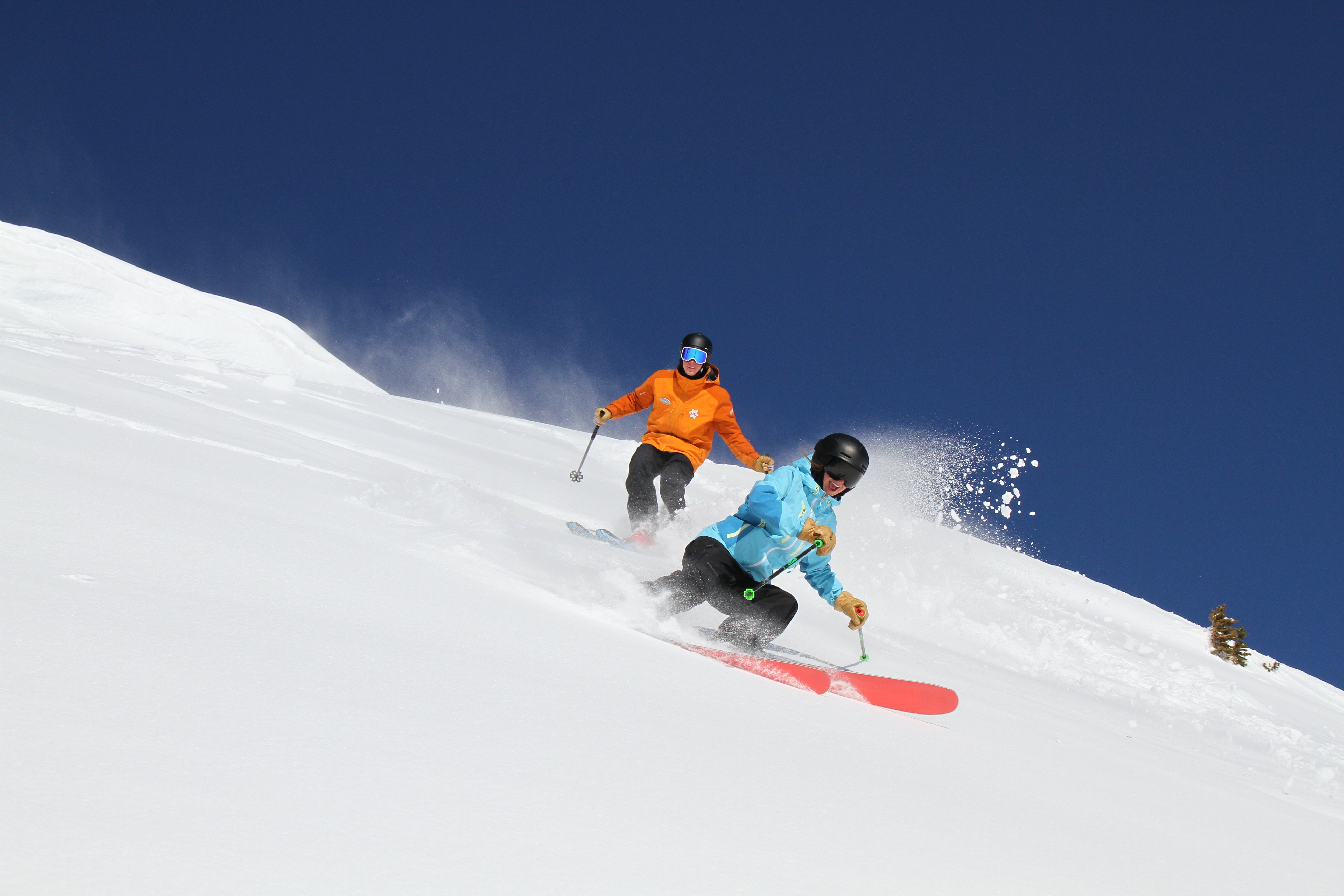 People skiing down steep slope on a bluebird day