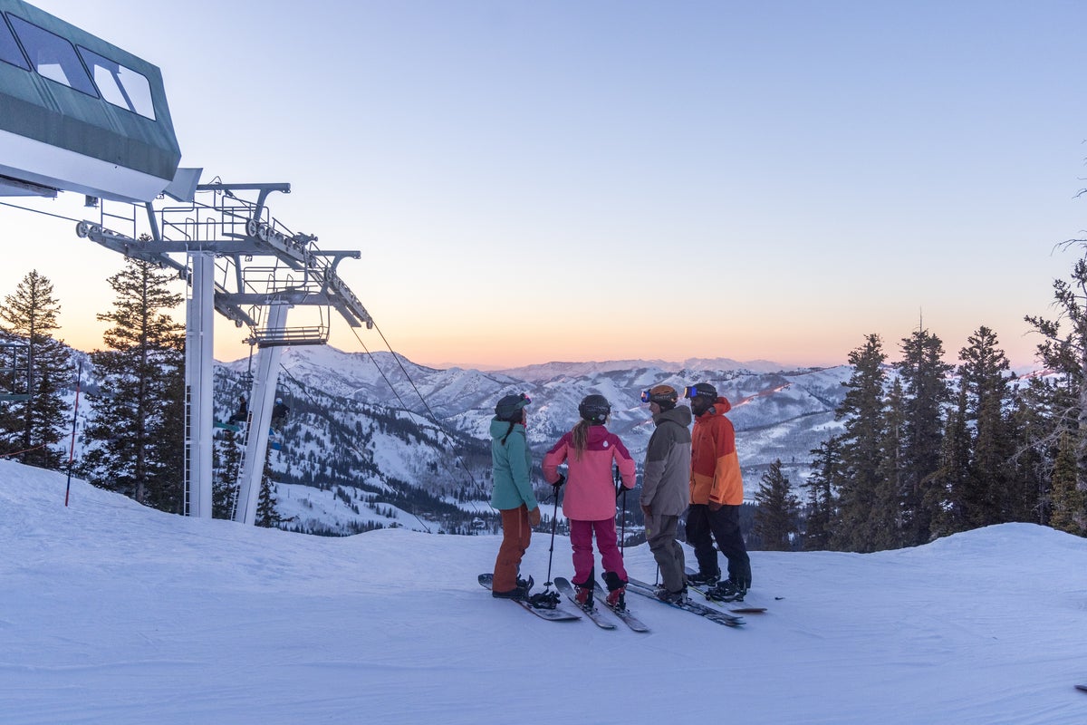 Group of friends on skis/snowboards beneath ski lift at sunset
