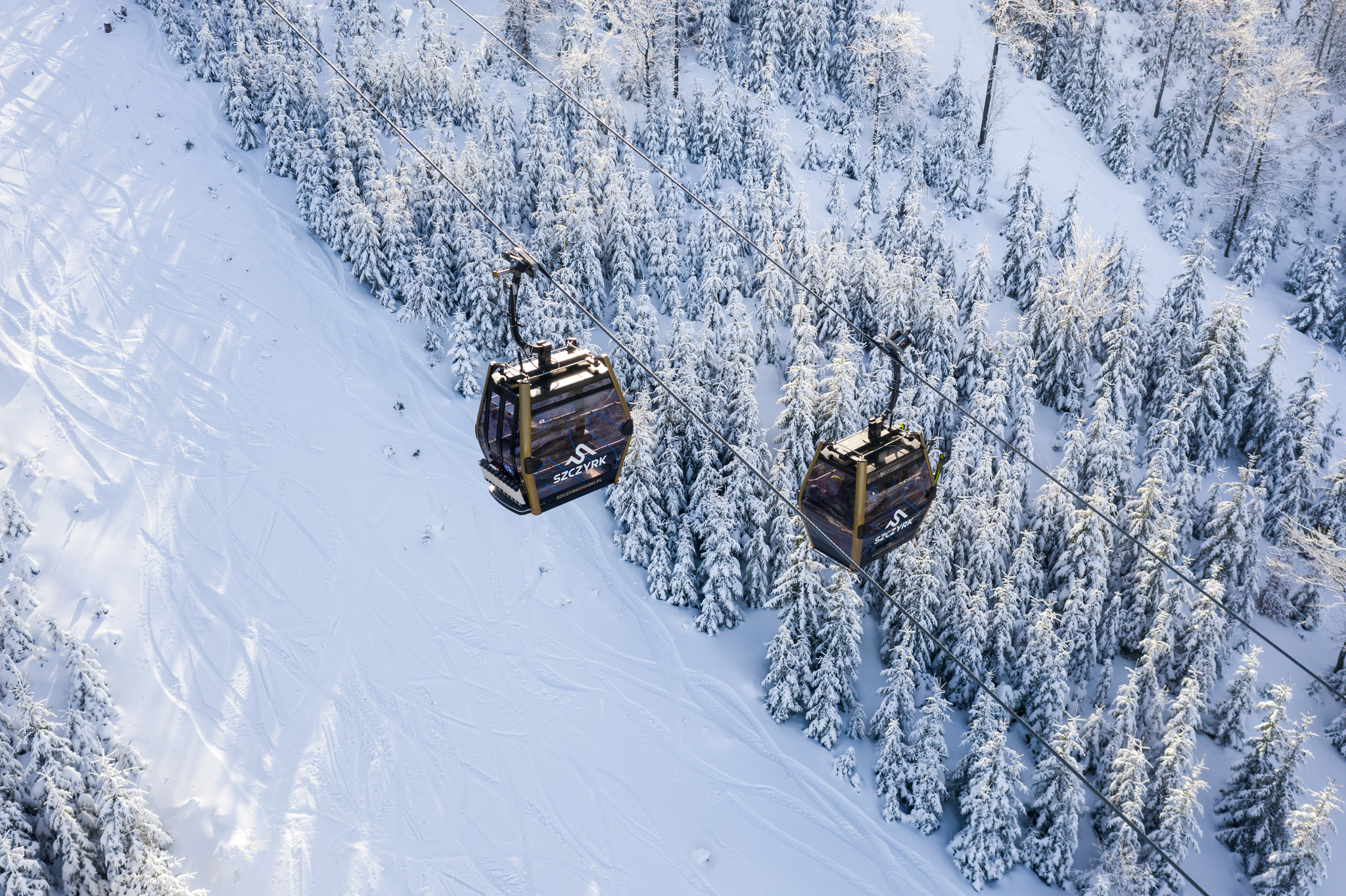 Kabiny lanovky nad zasněženým lesem ve Szczyrk Mountain Resort ve Slezských Beskydech