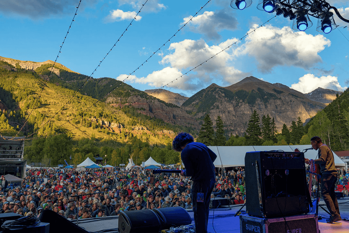 Band playing in front of large crowd on a sunny day with mountains in the background