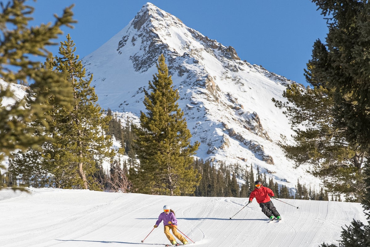 Skiing down groomed run on a sunny day at Crested Butte Mountain Resort with tall mountain behind them.