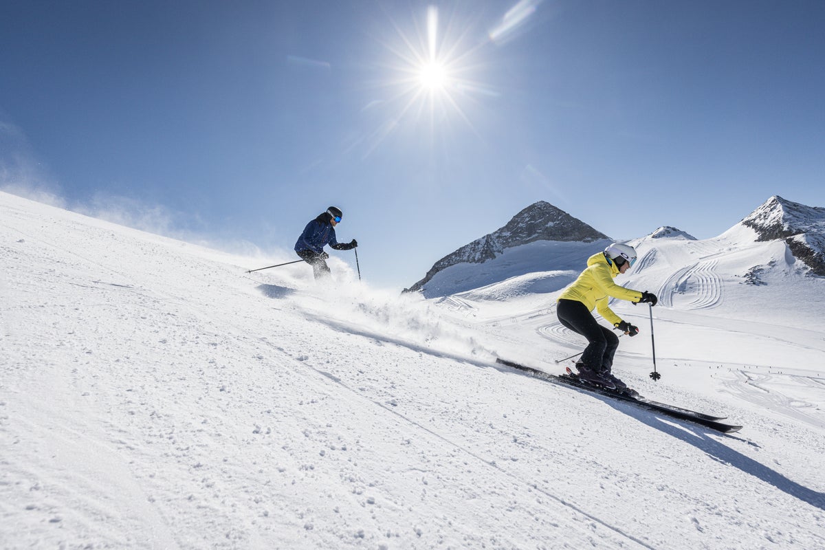 Two people skiing down groomed slopes on a sunny day