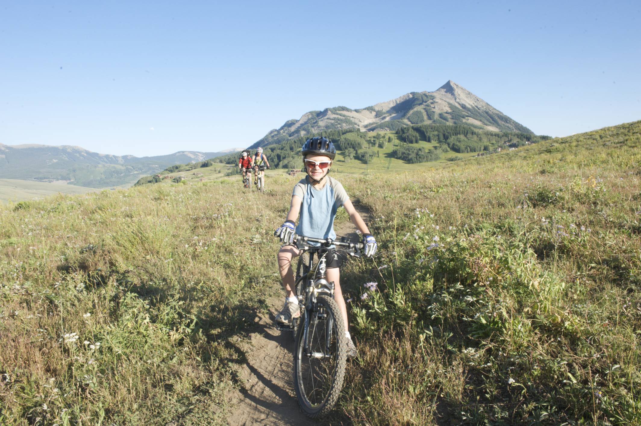A kid smiling while taking a break on a trail with her family riding behind her
