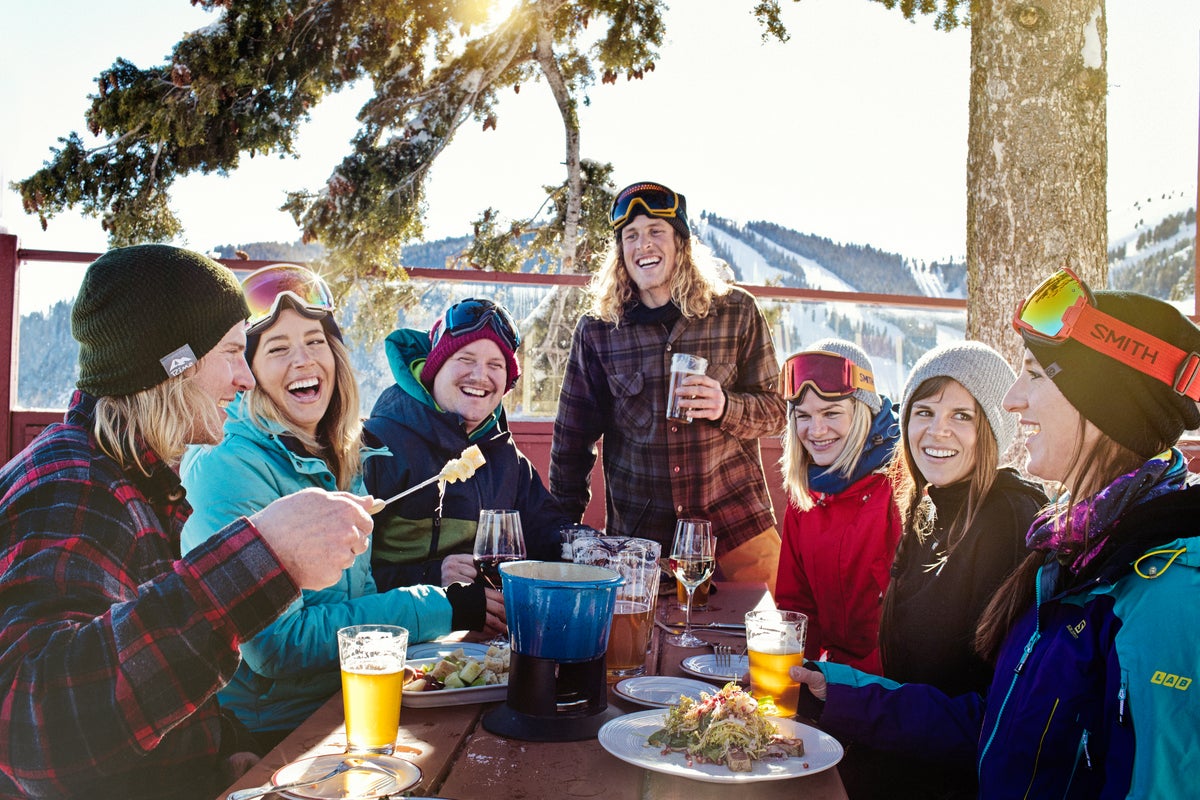 Friends enjoying a meal at Sun Valley Resort's Roundhouse Restaurant in Winter with the snow-covered mountains in the background