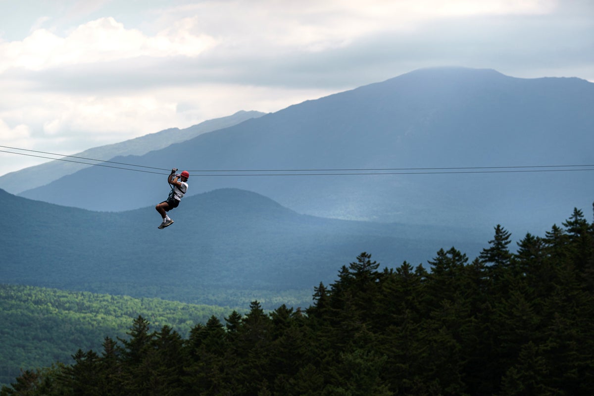 Person ziplining across zip line with mountains behind them