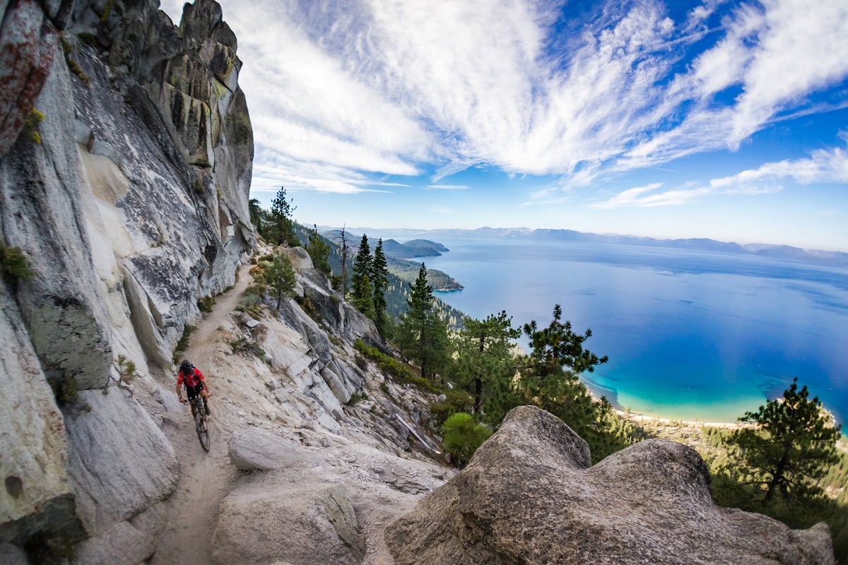 Person biking down a singletrack trail high above emerald lake below