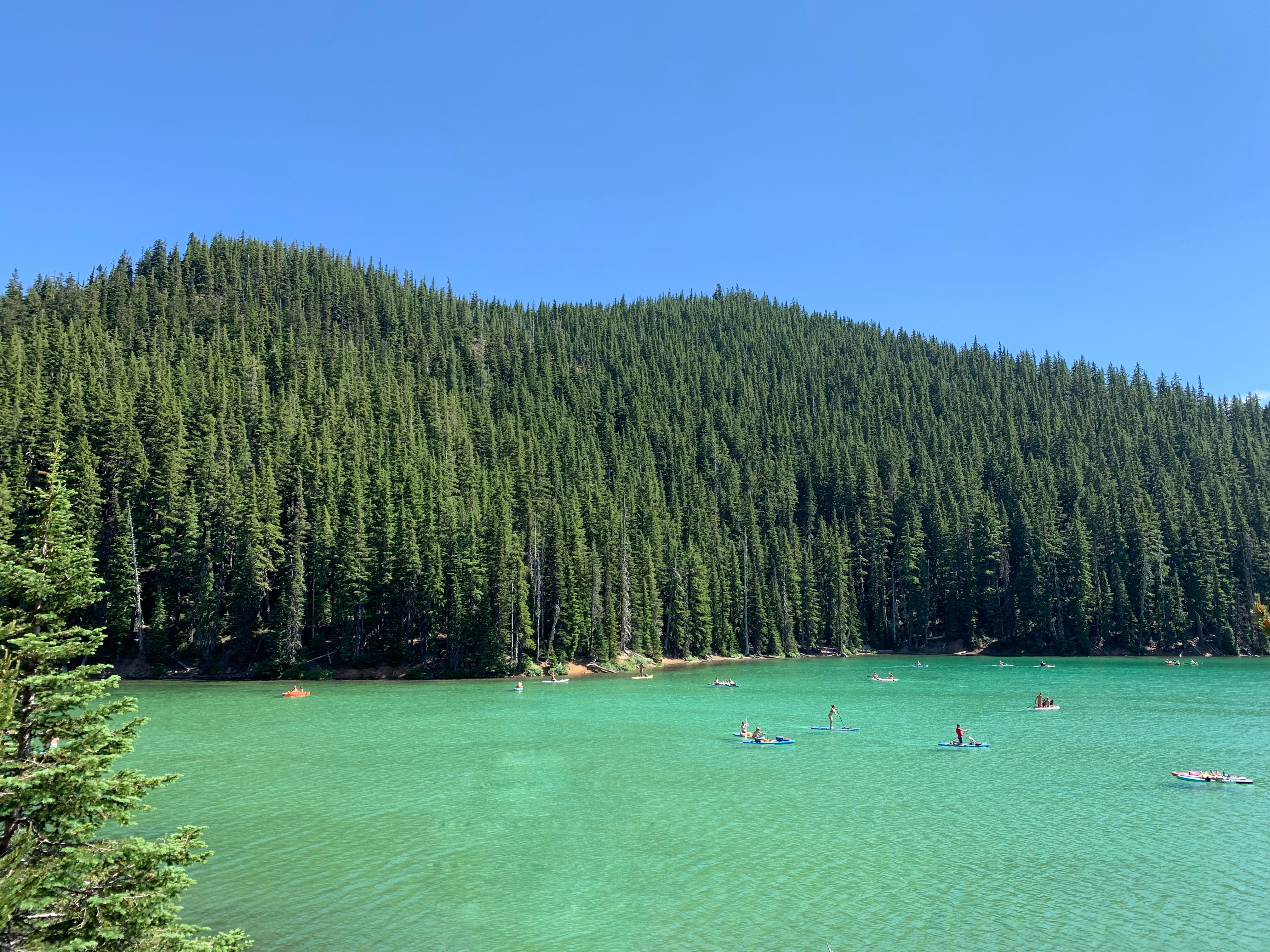 People kayaking and paddleboarding on emerald green lake on a sunny day in Central Oregon along the Cascade Lakes Scenic Byway 