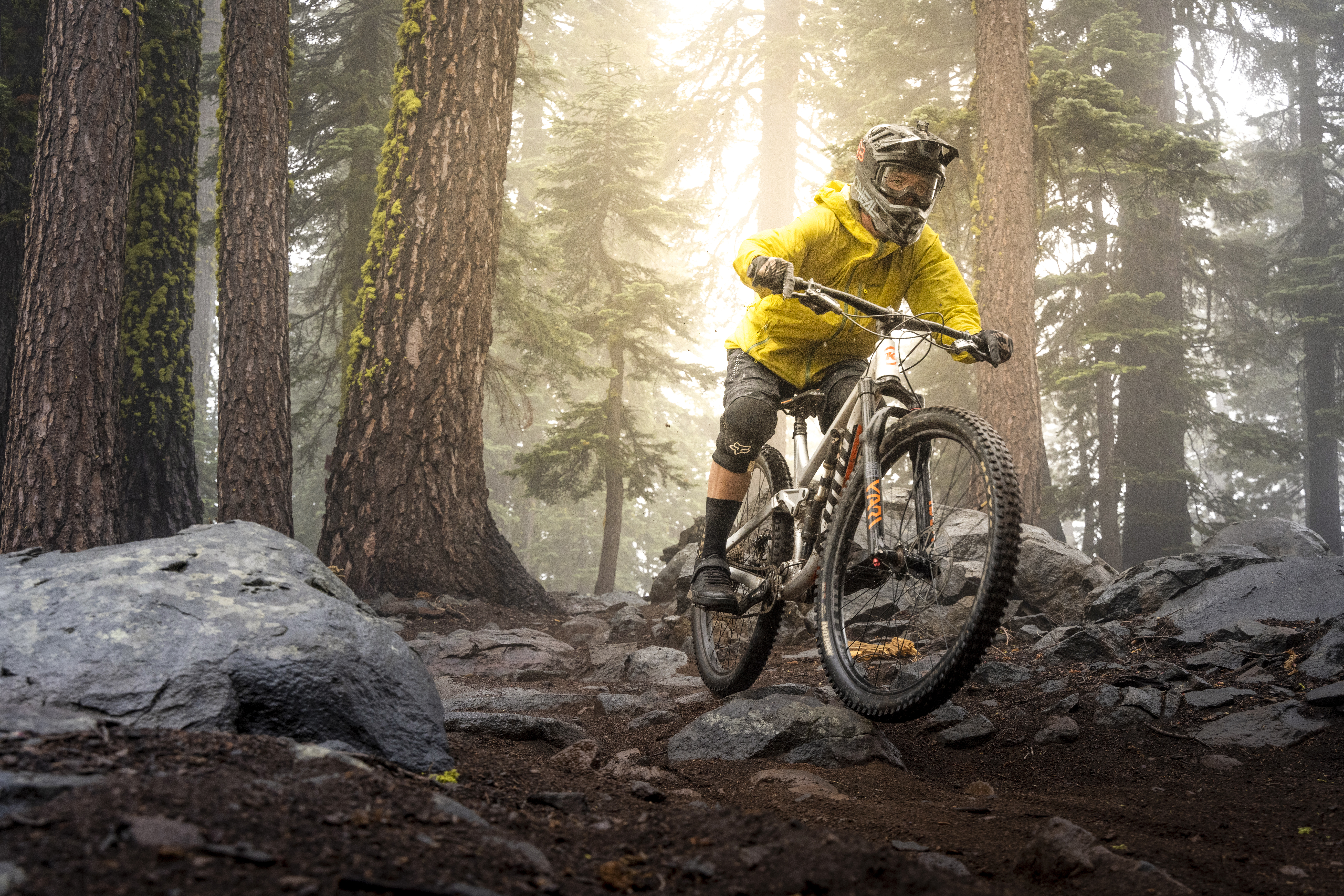 Biker with a helmet on riding along rocks in forest on a foggy day.
