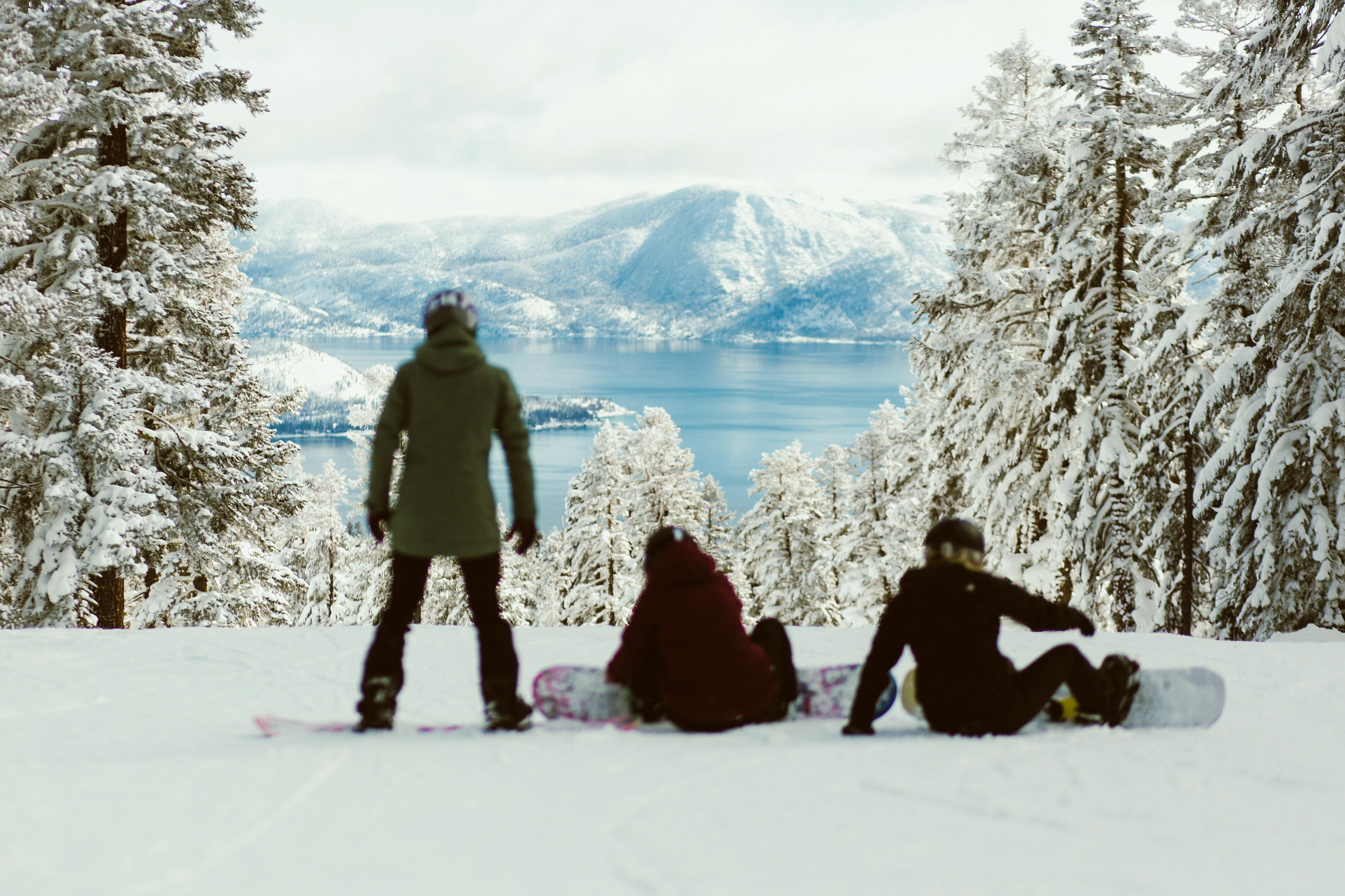 Group of friends strapping into snowboards on slopes overlooking Lake Tahoe