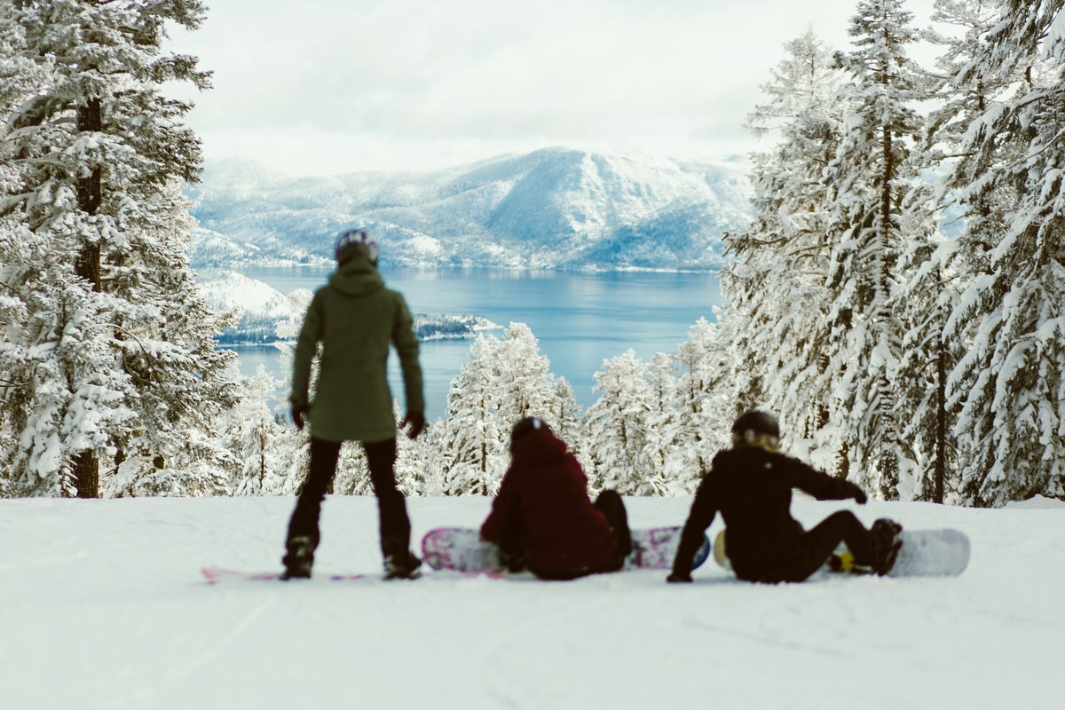 Group of friends strapping into snowboards on slopes overlooking Lake Tahoe