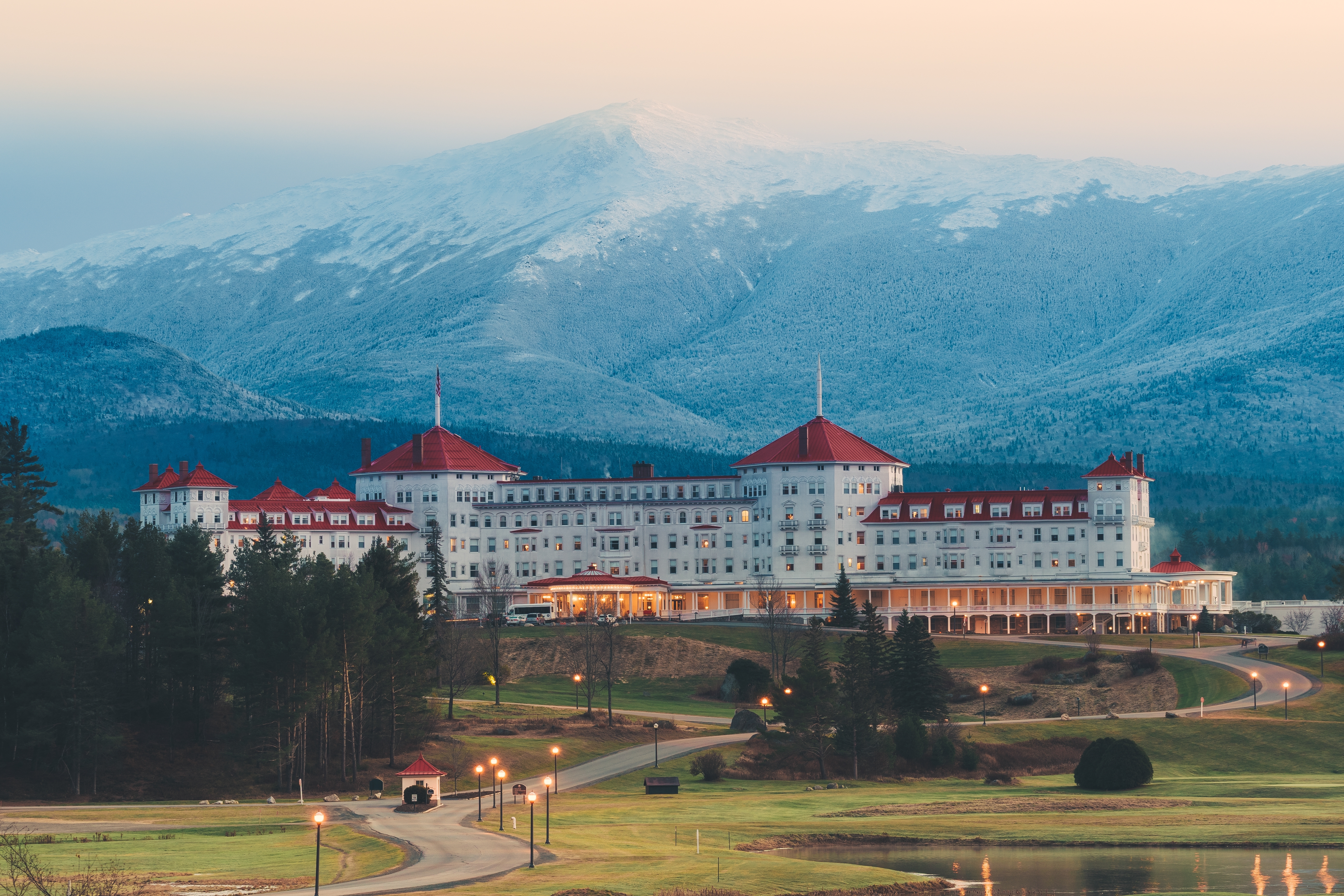 The Omni Mount Washington Resort at dusk with snow-dusted mountains behind it