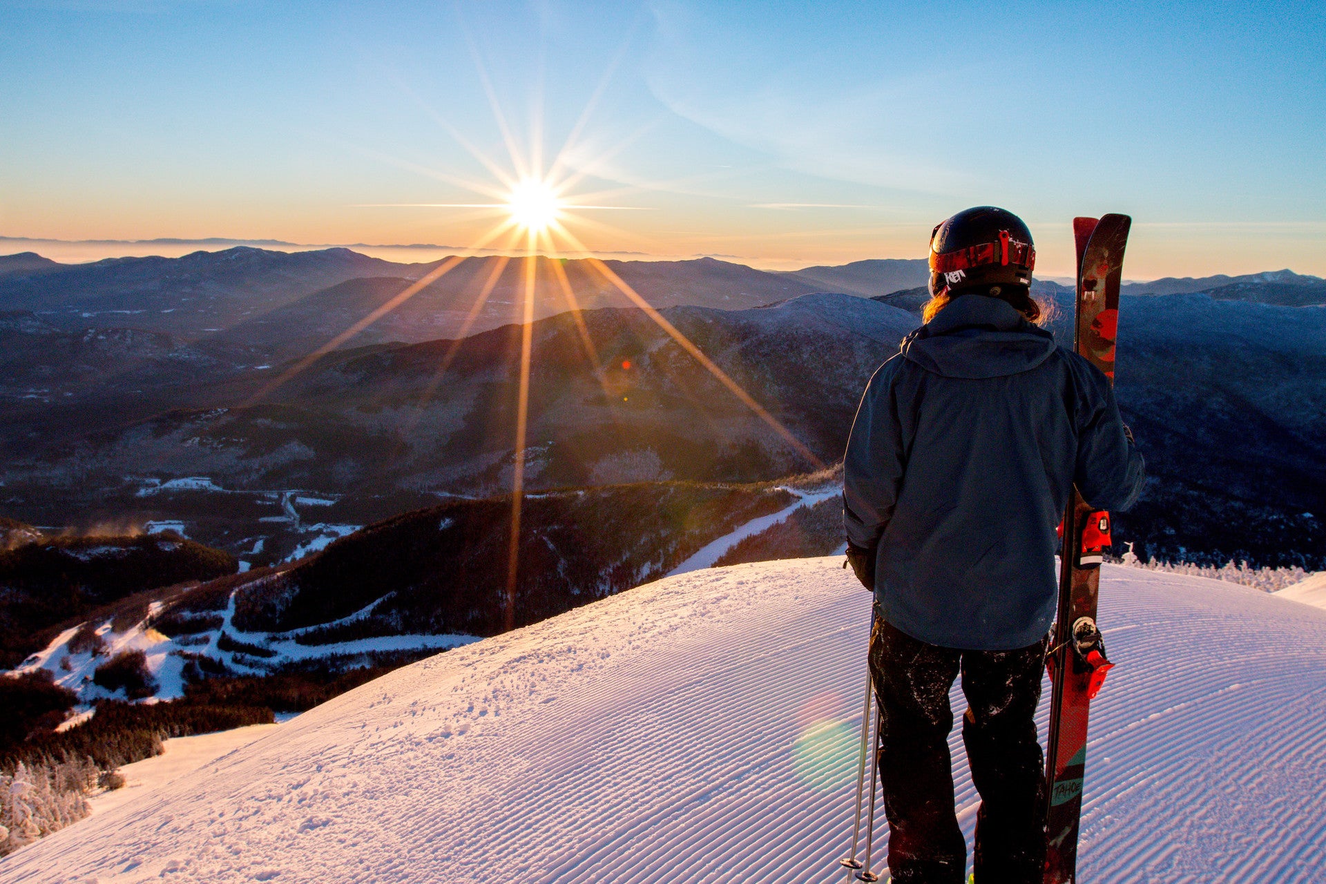 Person holding skis and watching sunrise over the mountains