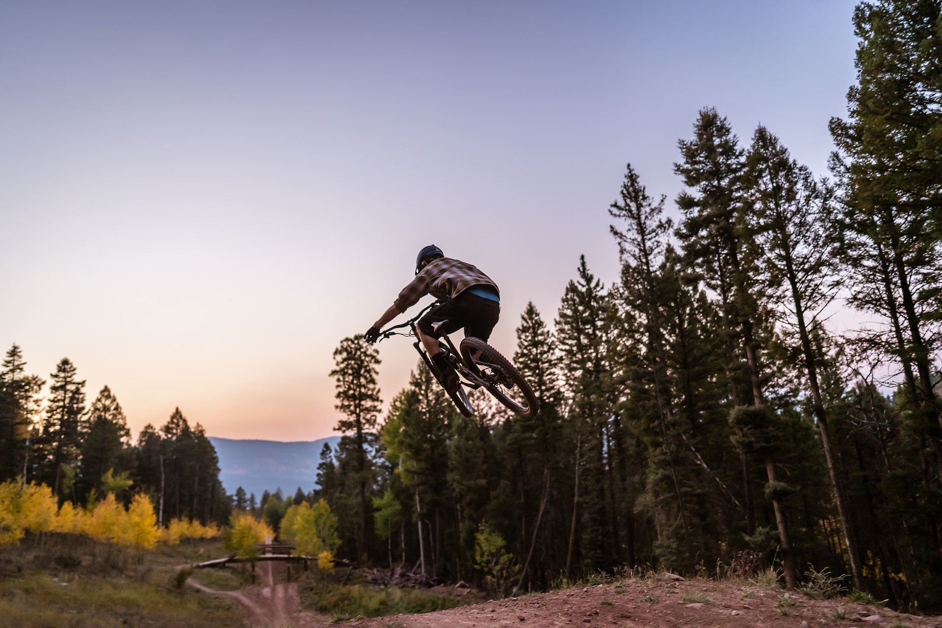 Biker getting air on a jump on mountain biking trail at dusk.