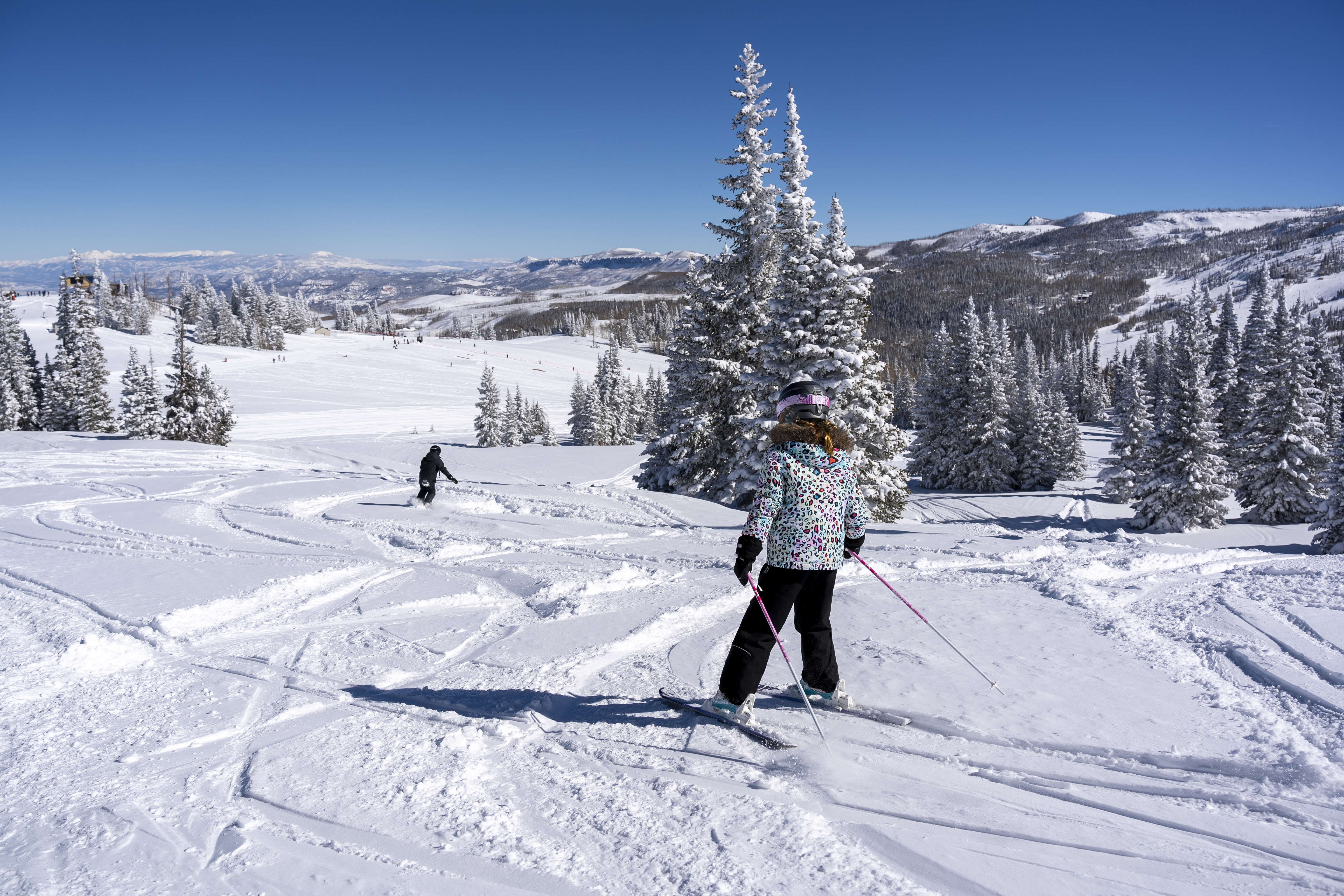 Two people skiing down blue run on a sunny day