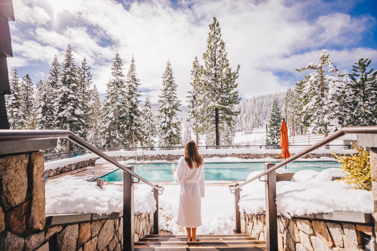 Person enjoying a drink by an outdoor pool surrounded by snow-covered trees