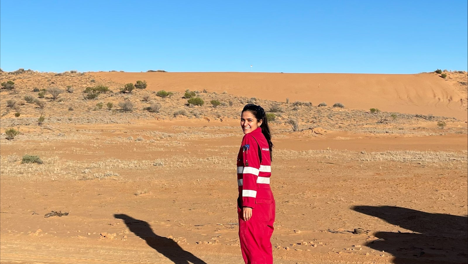 Halliburton employee wearing red Halliburton rig coveralls in a sandy environment.