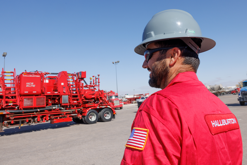 Halliburton employee on rig site with cementing trucks around him.