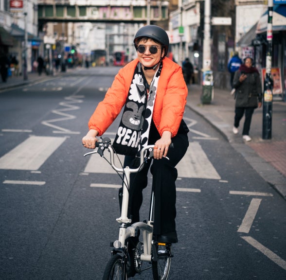 A happy person in an orange jacket riding a Brompton A Line