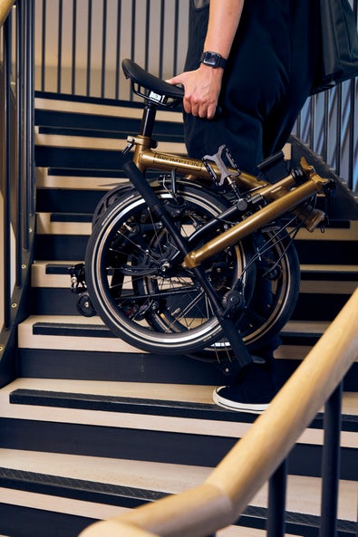 A person carrying a folded Brompton P Line up a set of stairs towards the Empire State Building
