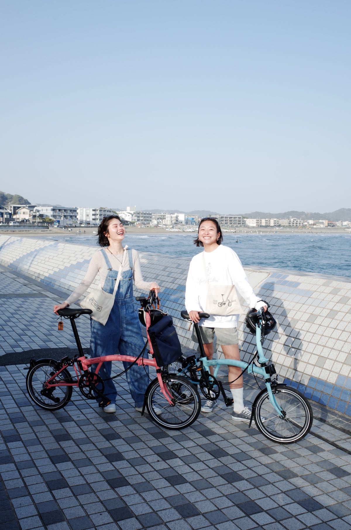 カフェの外でテーブルに座っている2人組が、飲み物と折りたたまれたBrompton自転車を並べています。