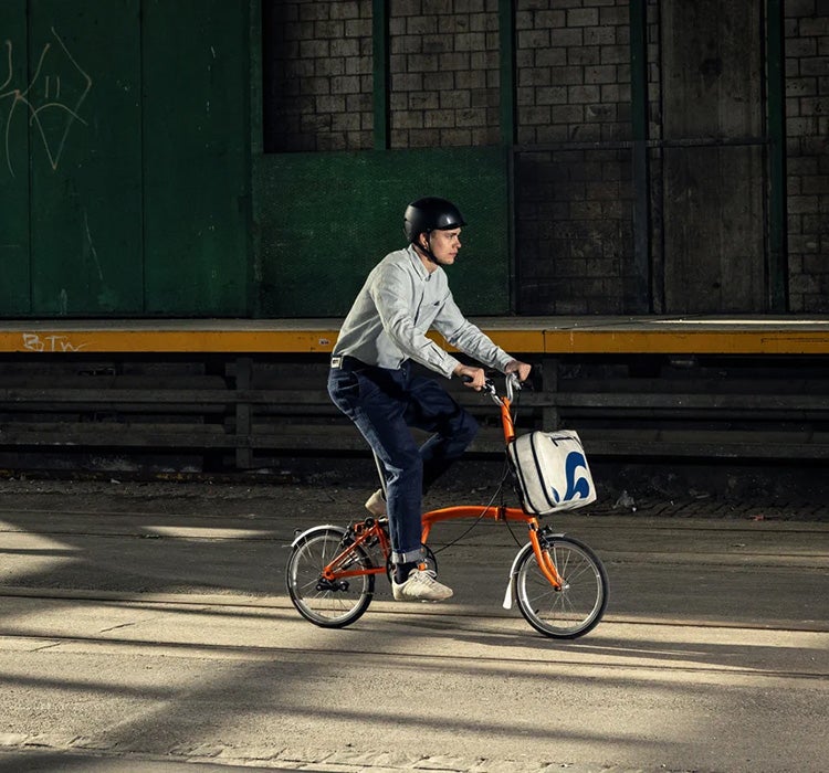 Un homme conduisant un Brompton avec un sac Freitag x Brompton attaché au bloc à bagages