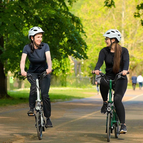 Two people riding Brompton bikes along a path